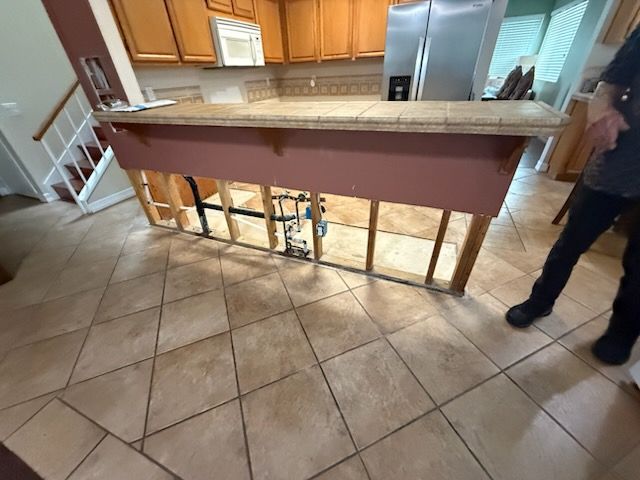 Kitchen under renovation with exposed island framing and tiled floor; person standing at right.