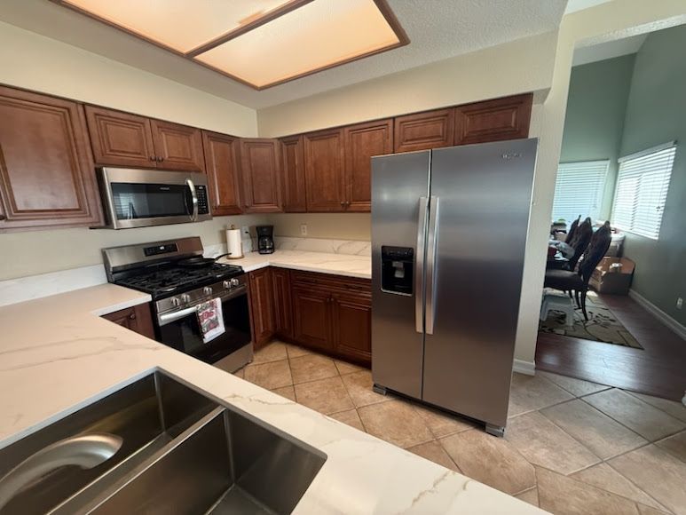 Modern kitchen with wood cabinets, stainless steel appliances, and tile flooring, viewed from the sink.