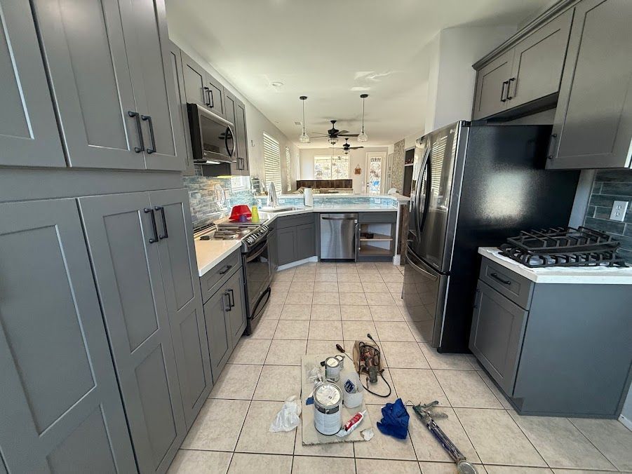 Modern kitchen with gray cabinets, black appliances, tiled floor, and cleaning supplies on the floor in the center
