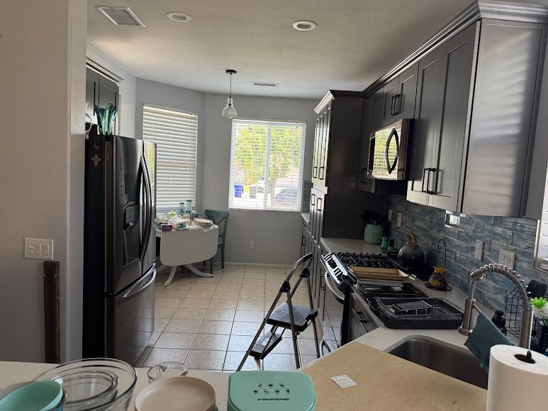 Modern kitchen with dark cabinets, stainless appliances, and a tripod near the stove and sink
