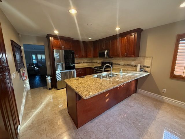 Modern kitchen with dark wood cabinets, granite island, stainless appliances, and beige tile floor