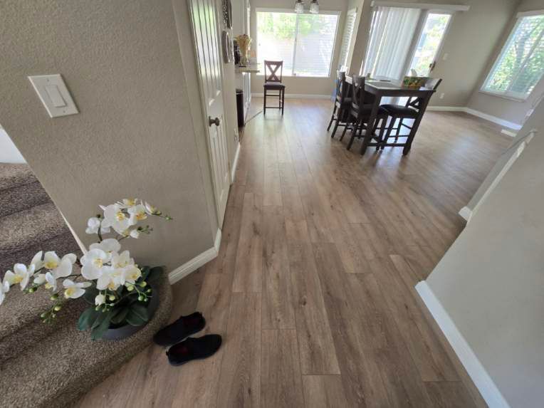 Bright living and dining area with wood floors, chairs, table, staircase, and white flowers by the entryway