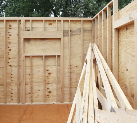 Wood-framed room under construction with plywood walls and stacked lumber inside