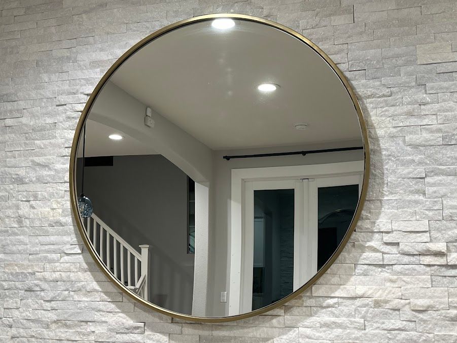 Round wall mirror reflecting a staircase and white interior ceiling lights on a stone-textured wall