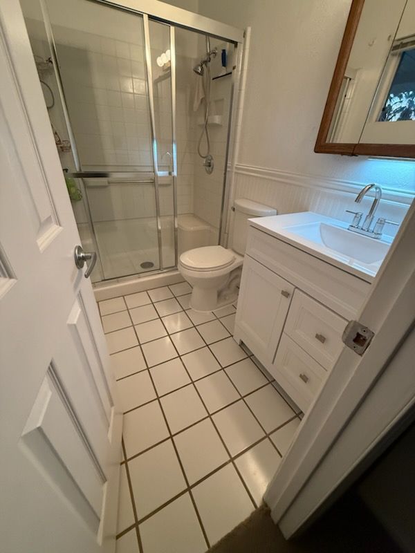 Small white bathroom with shower, toilet, and vanity sink viewed from the doorway