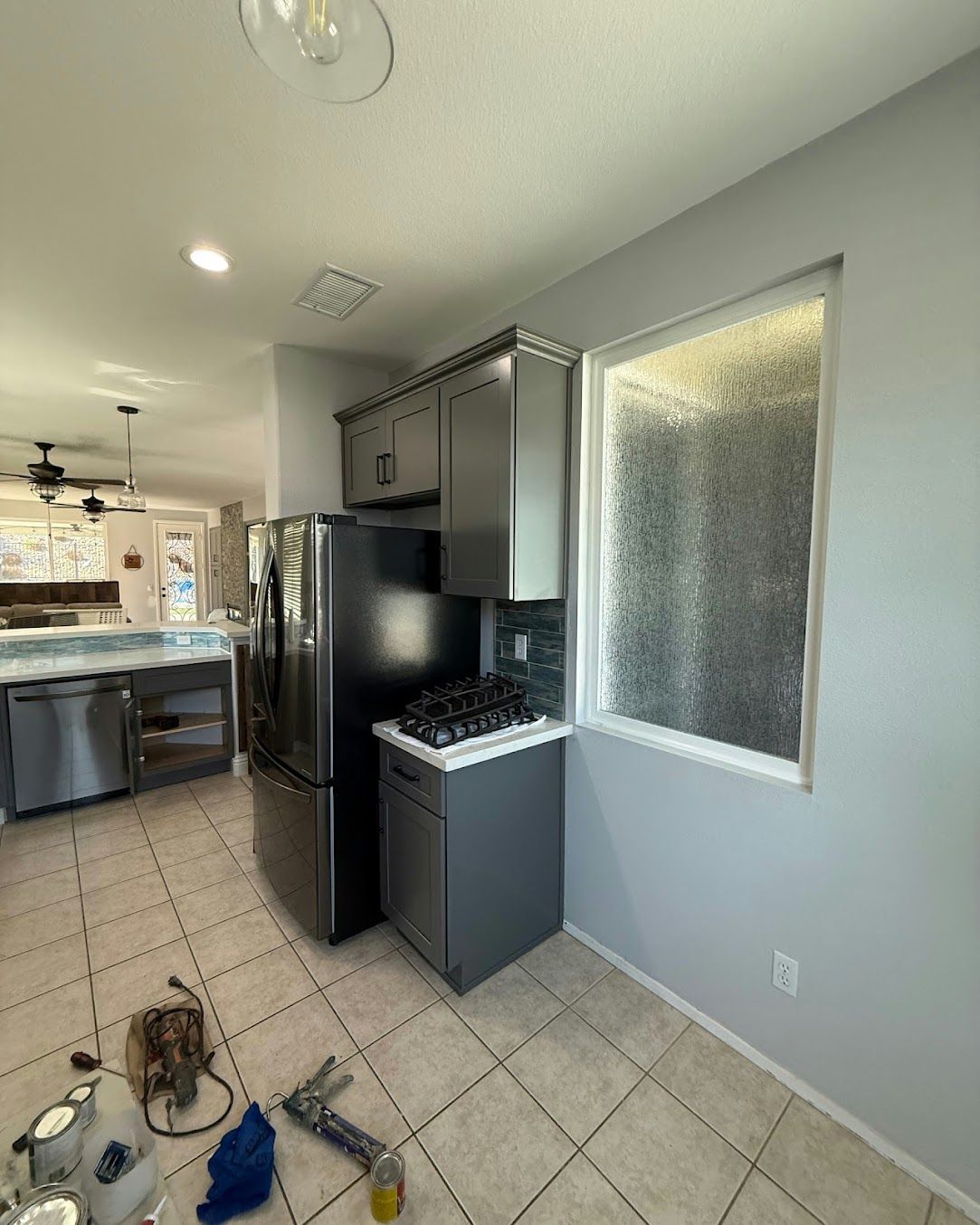 Small kitchen with black appliances, tiled floor, and frosted window in a narrow hallway.