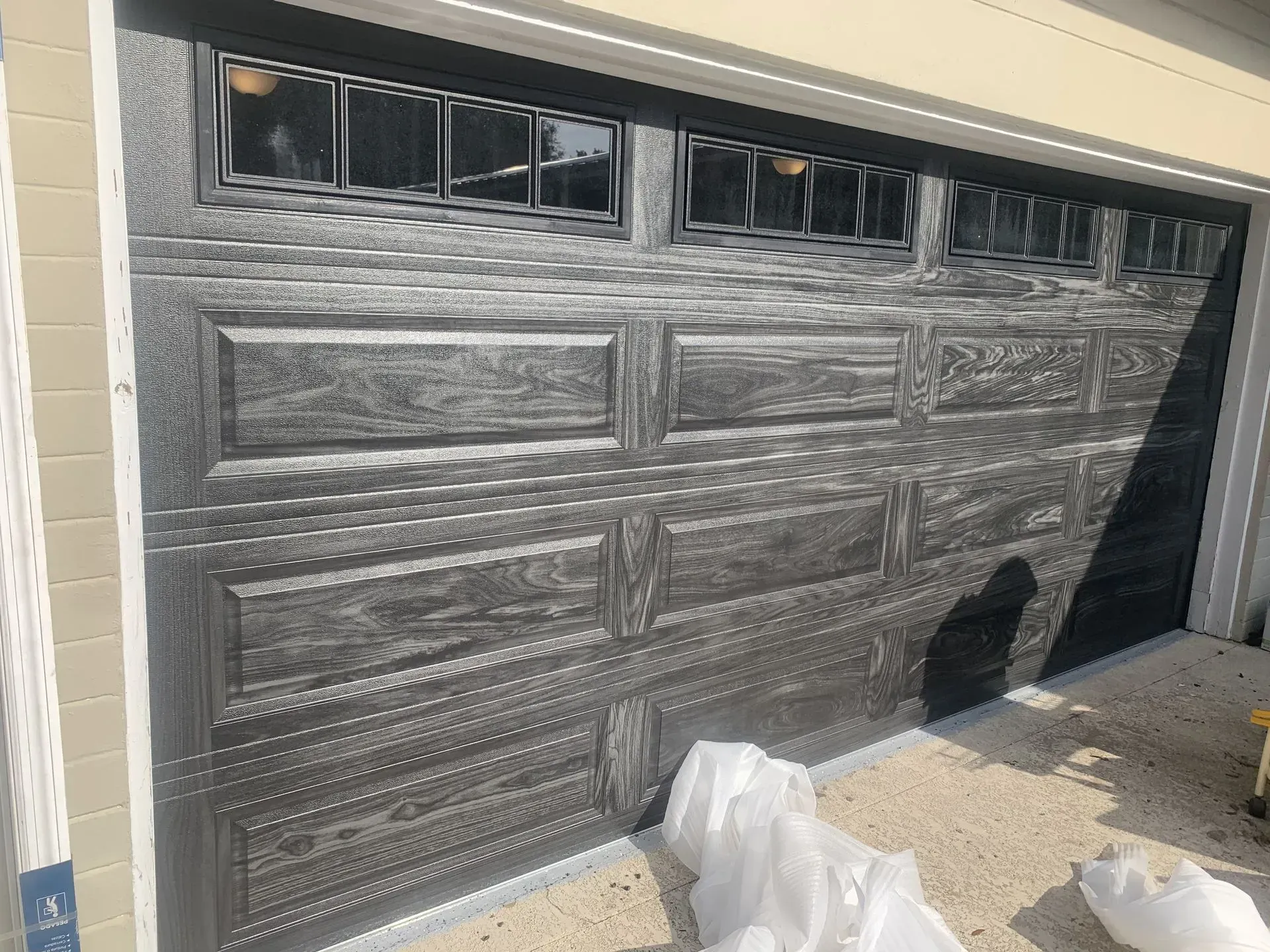 Dark gray garage door with panels and window inserts. White plastic covers the floor.