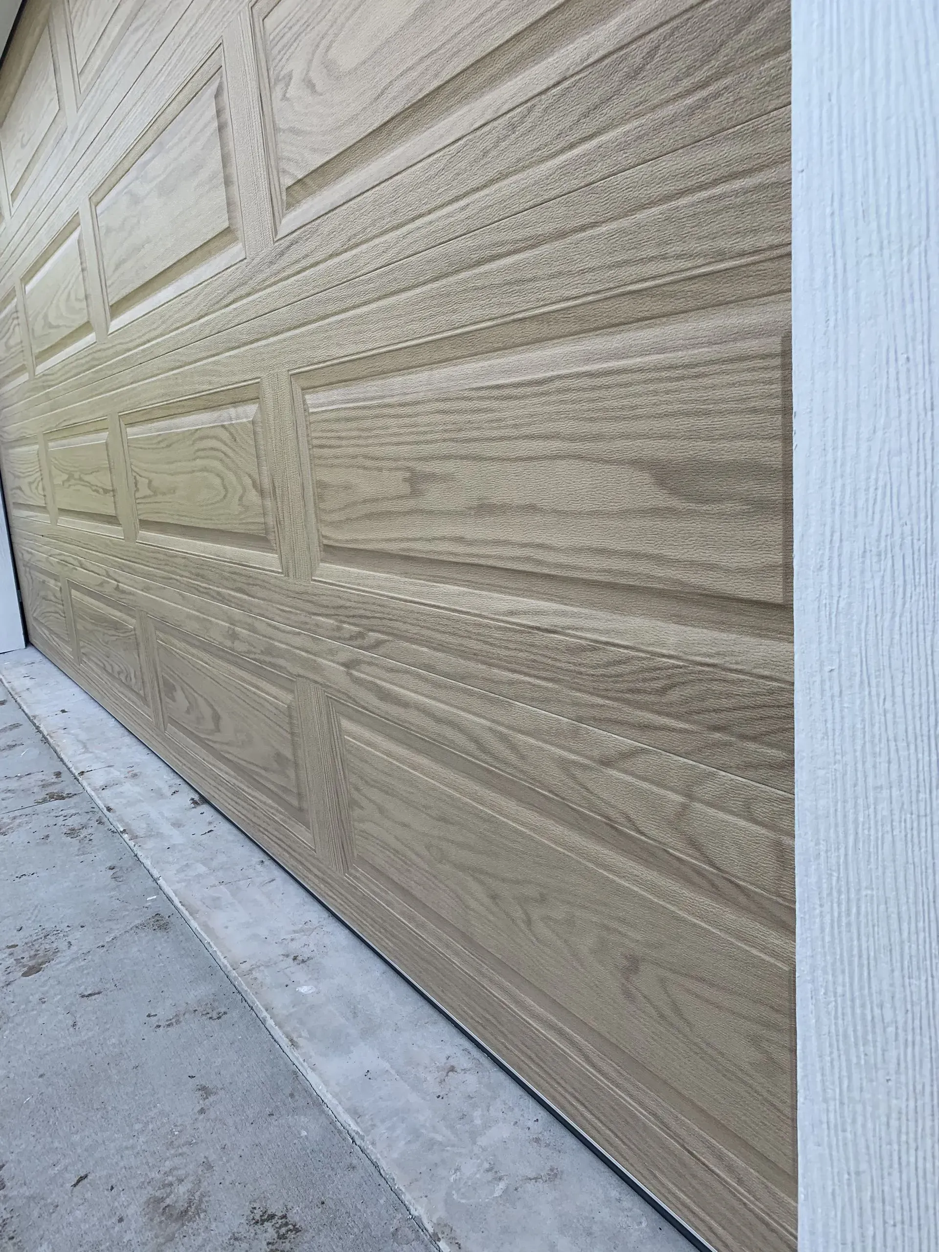 Tan textured garage door close-up, with concrete base and white trim on the right.