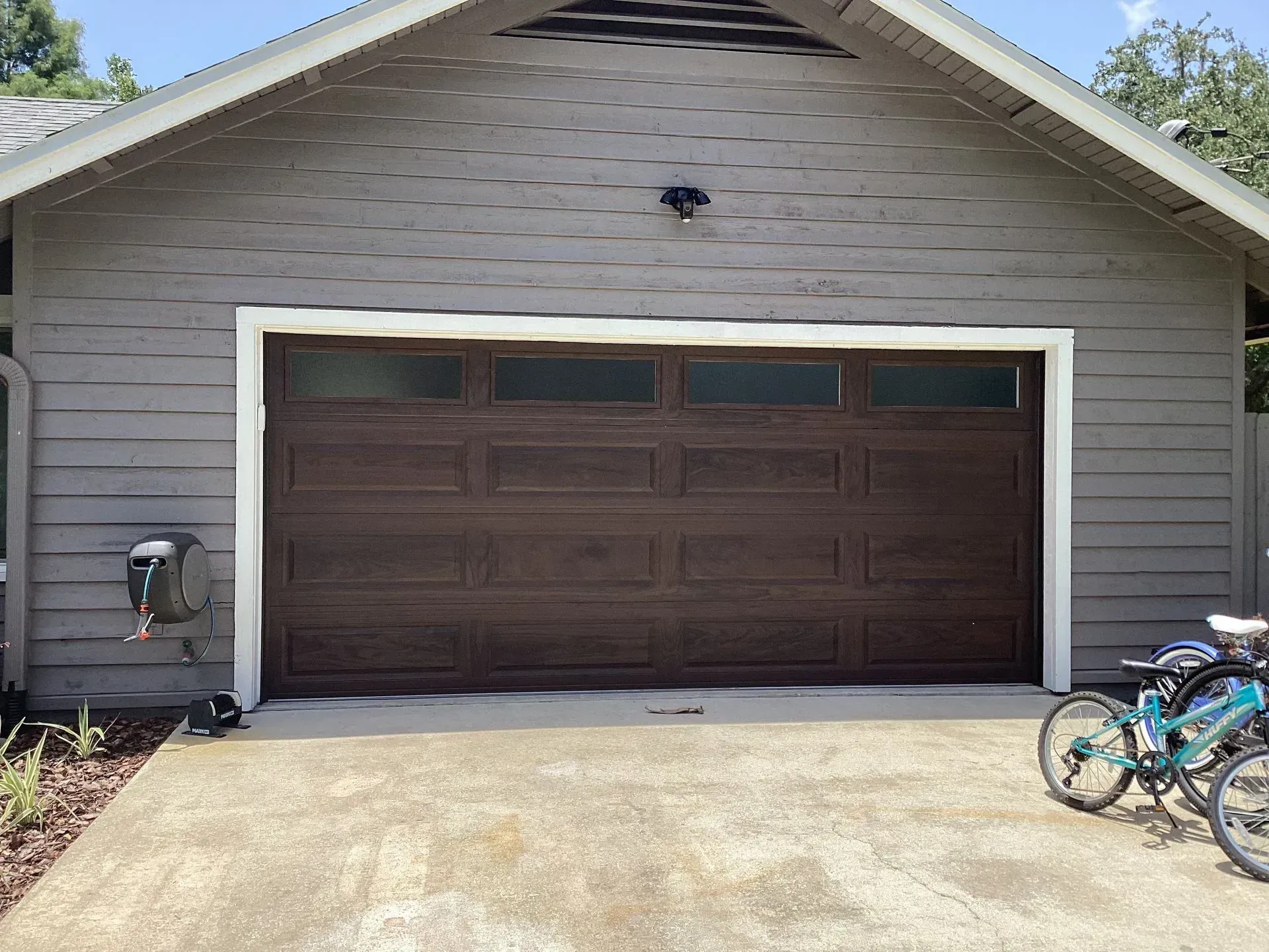 Brown garage door with windows, gray siding, and a concrete driveway.