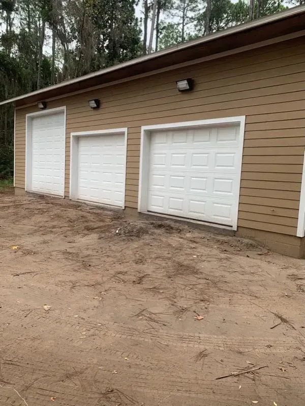 Three white garage doors on a tan building with brown trim; dirt ground.