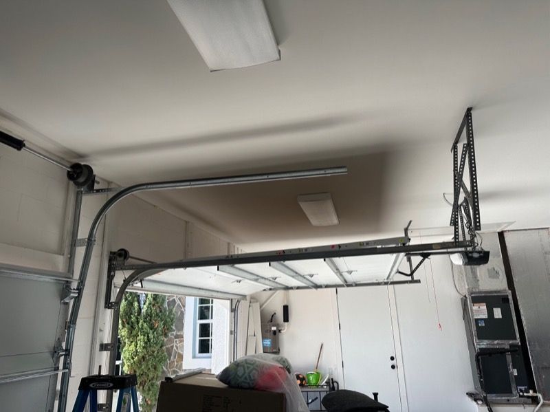 Garage door track, rails, and opener mechanism installed on a white ceiling. The door is partially open.