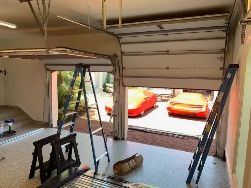 Garage with open door, showing two red cars. Ladders and sawhorses are inside the garage.