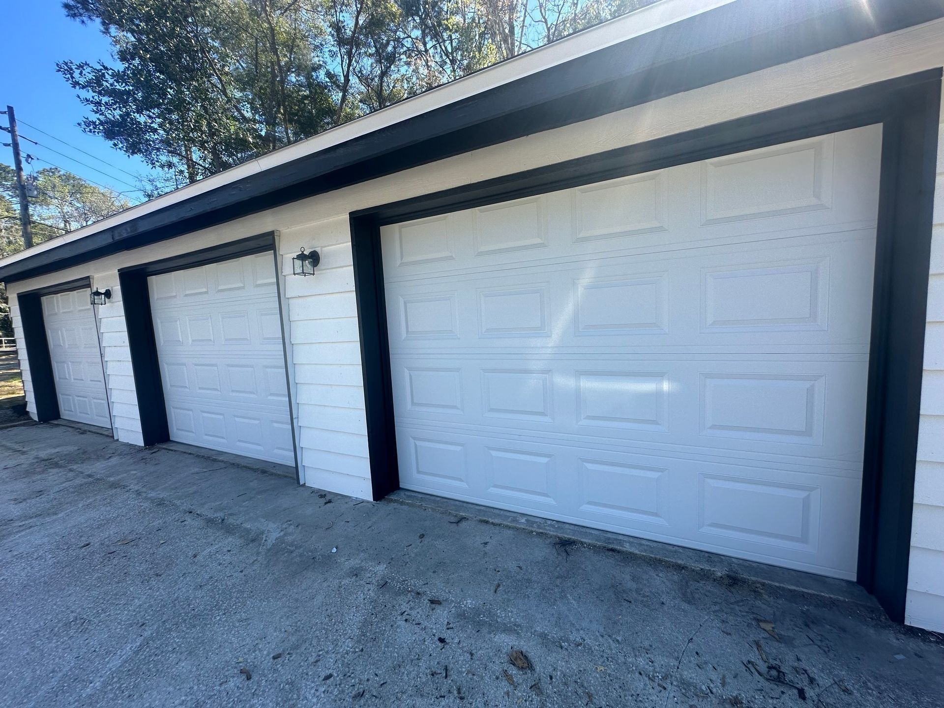 Three white garage doors with black trim, concrete driveway.