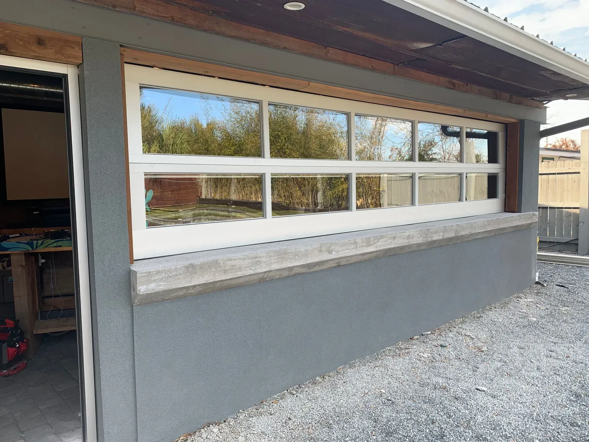 White-framed window with multiple panes on a gray stucco wall, reflecting trees.