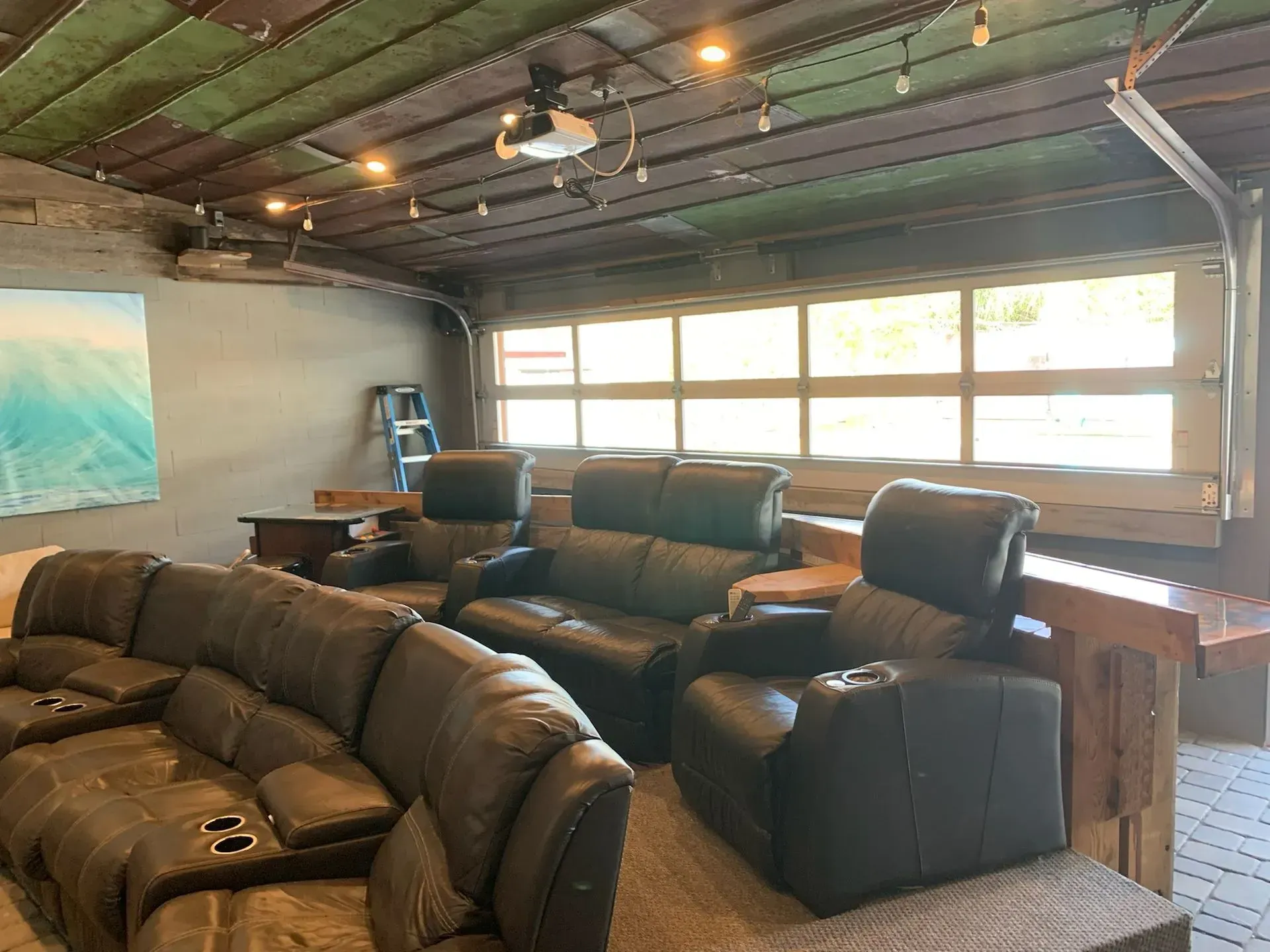 Home theater with leather seating, projector, and garage door windows. Rustic ceiling and bar.