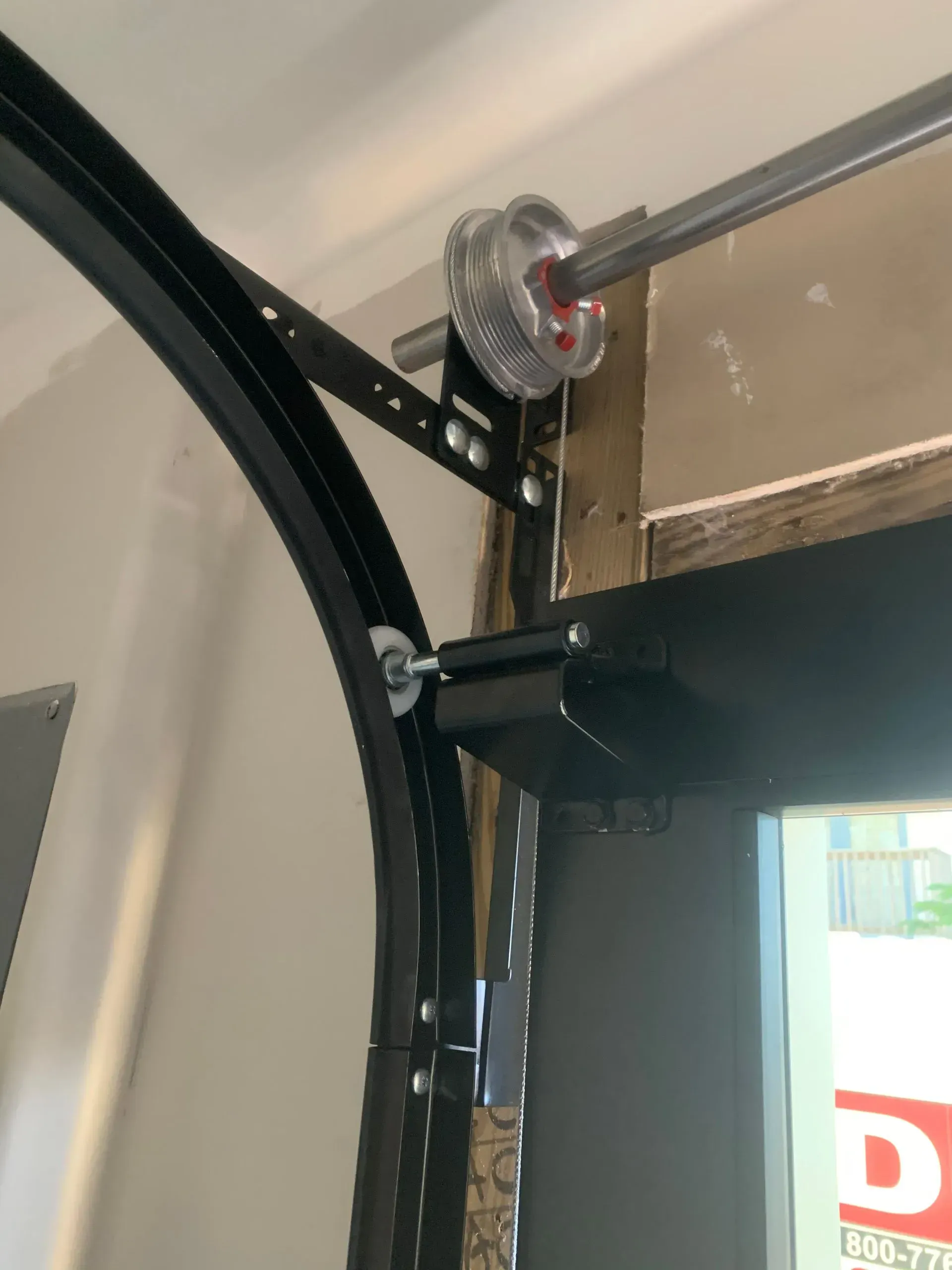 Garage door track and cable system. Black curved track with roller and cable drum.