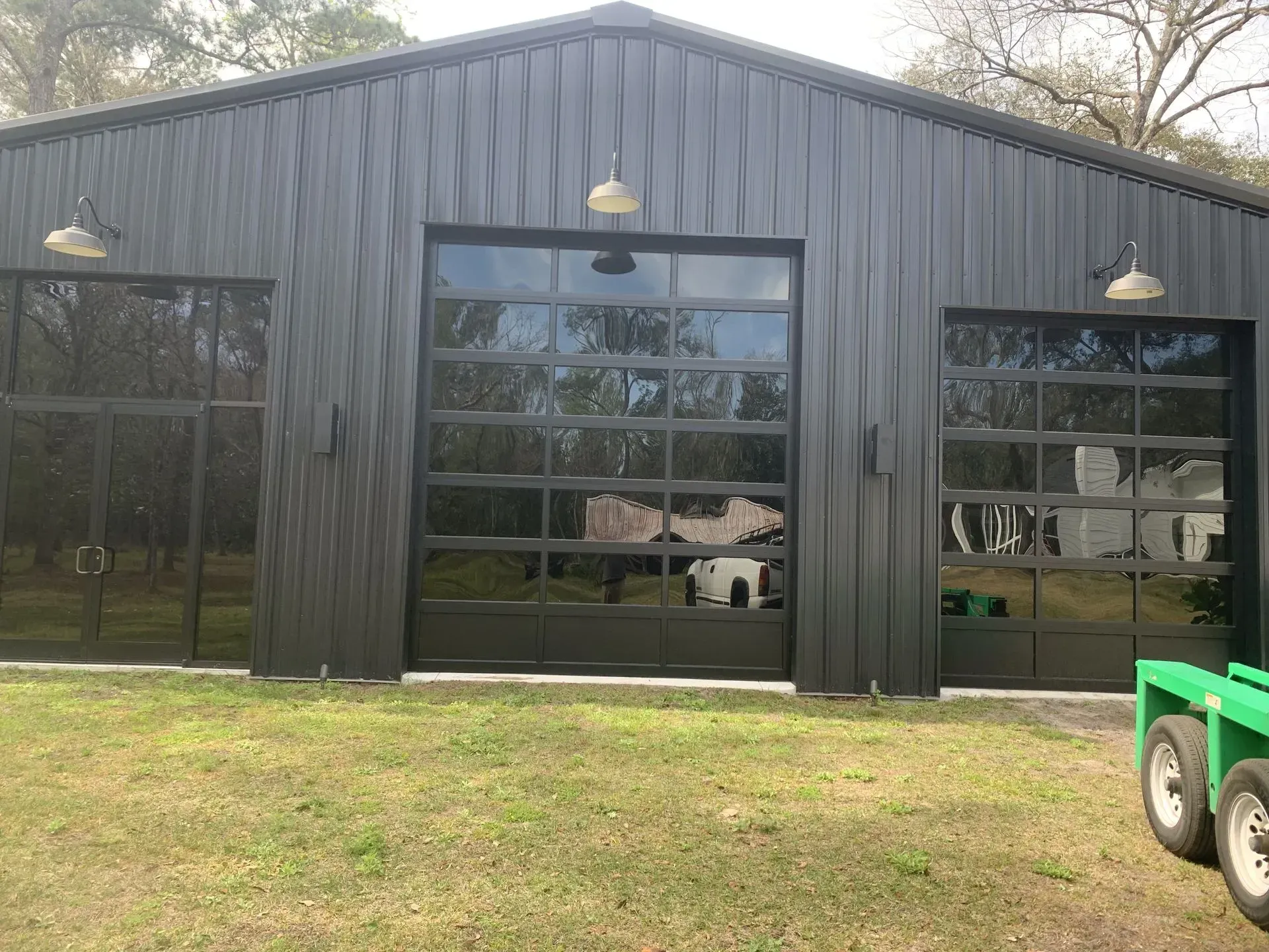 Black metal building with three garage doors. Exterior lights and green grass visible.