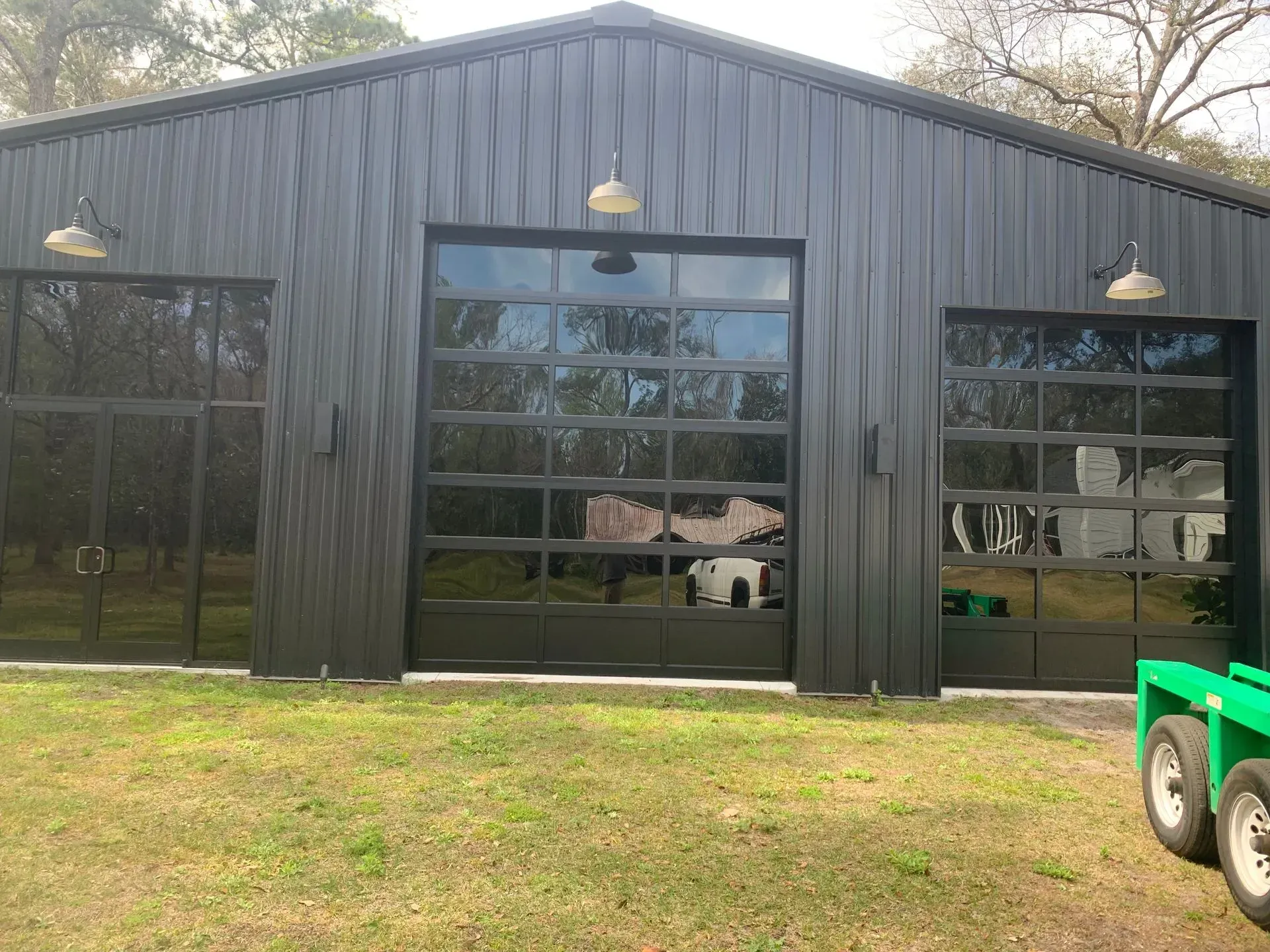 Black metal building with three glass doors, outdoor lights, and green grass.