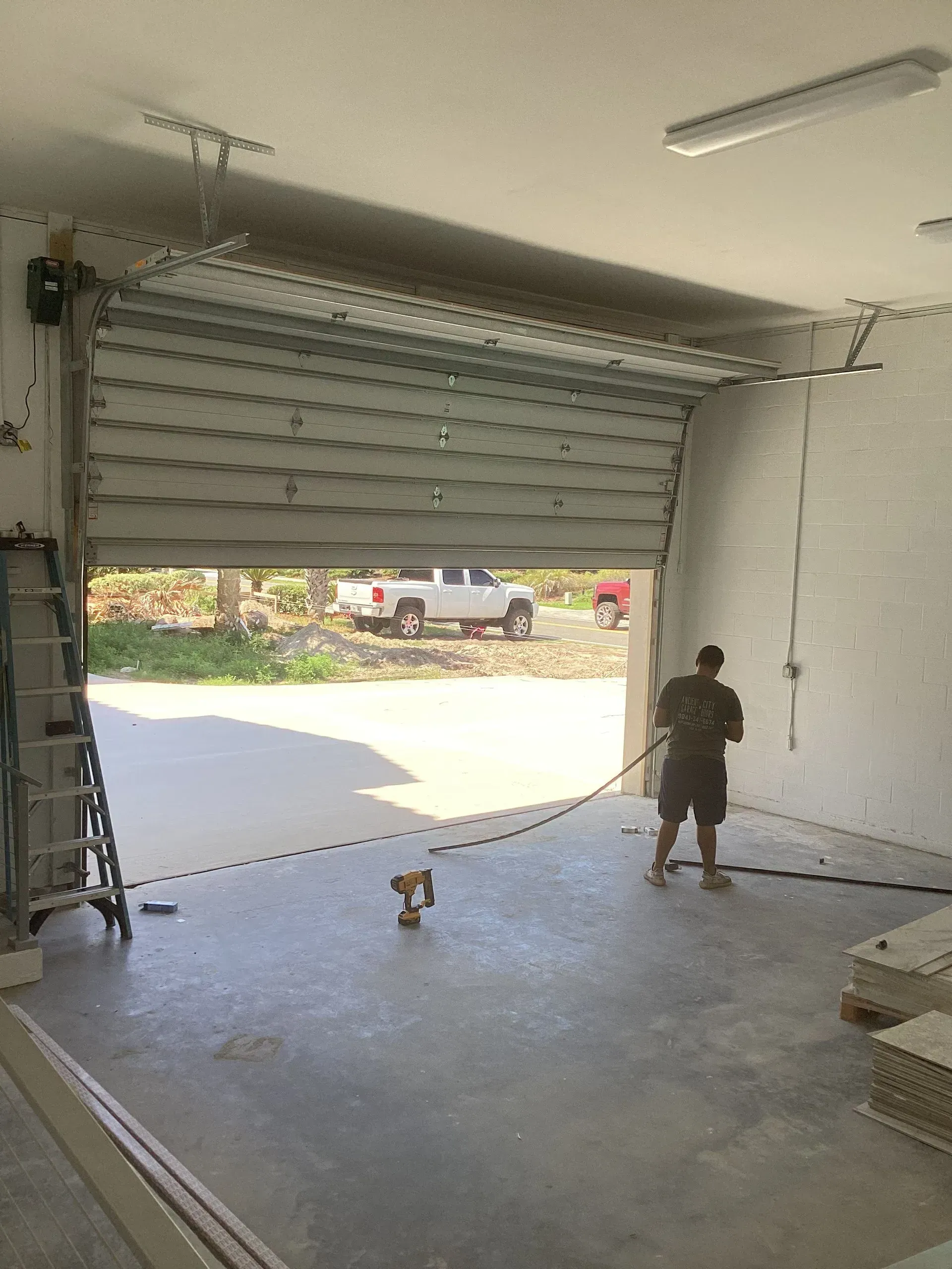 Man in a warehouse testing a garage door with a truck visible outside. Gray door, concrete floor.