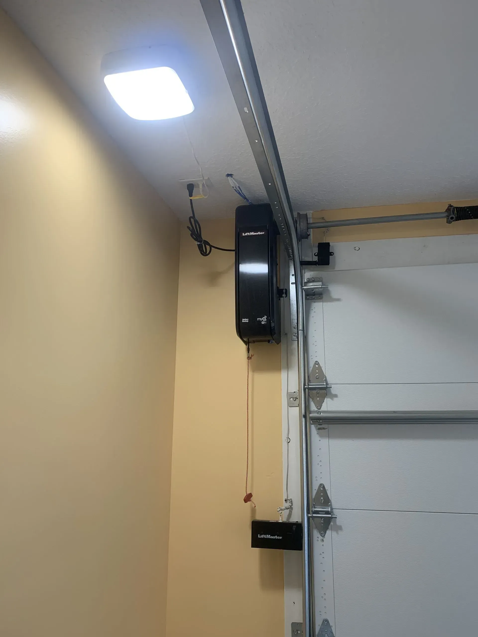 Garage door opener with light and track attached to the ceiling above a closed garage door.