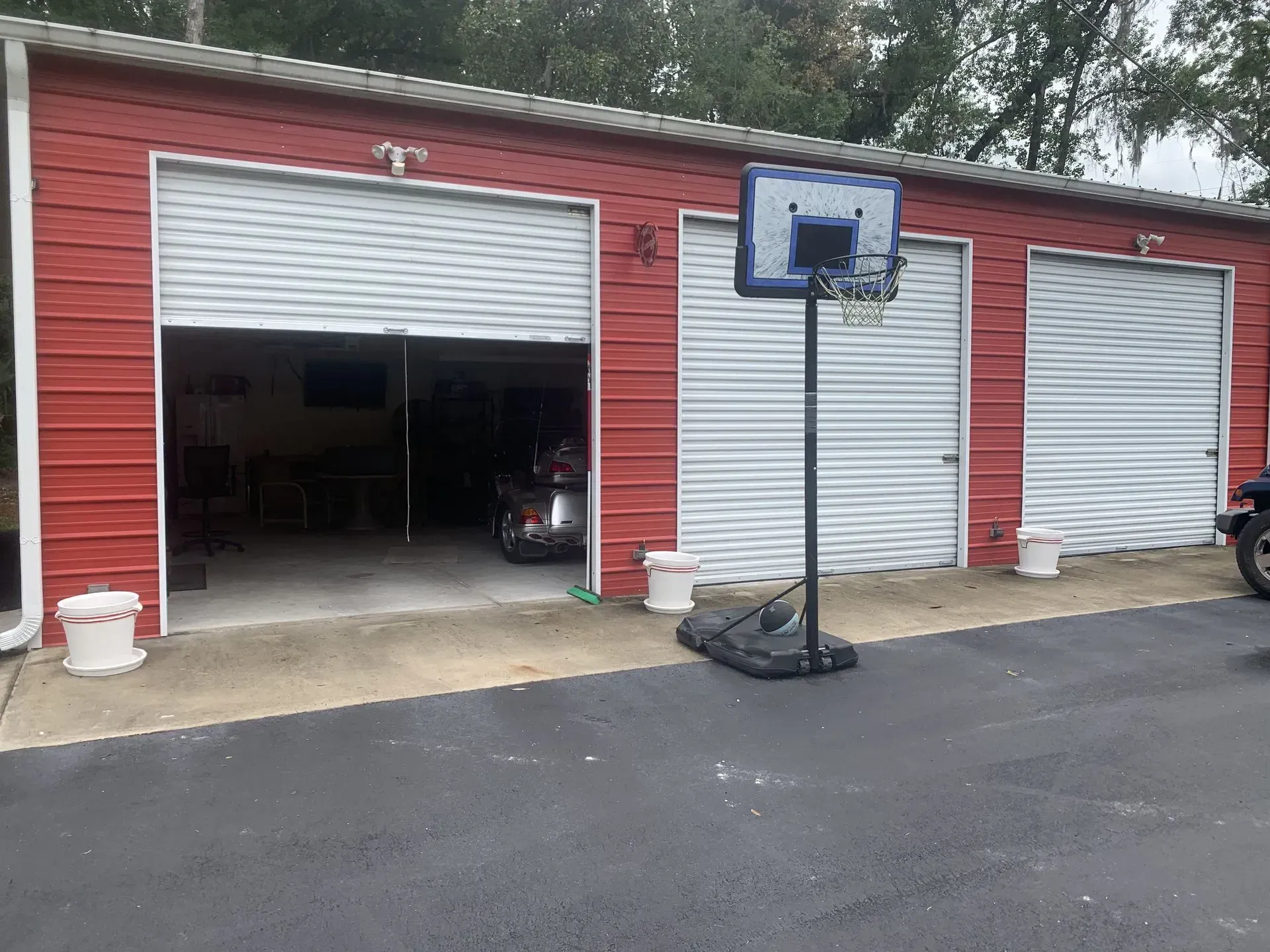 Red storage units with open door, basketball hoop, and asphalt driveway.