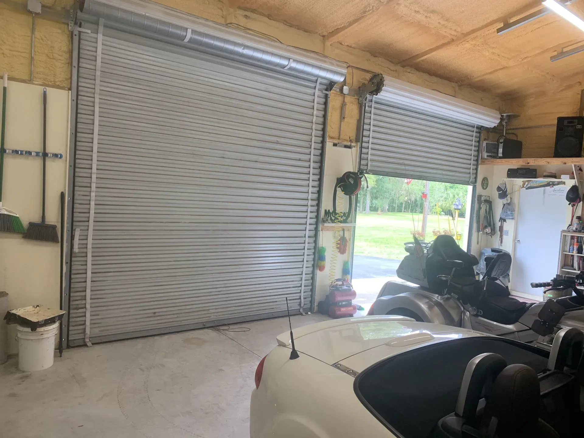 Garage interior with two gray roll-up doors, one partially open, and a white car.