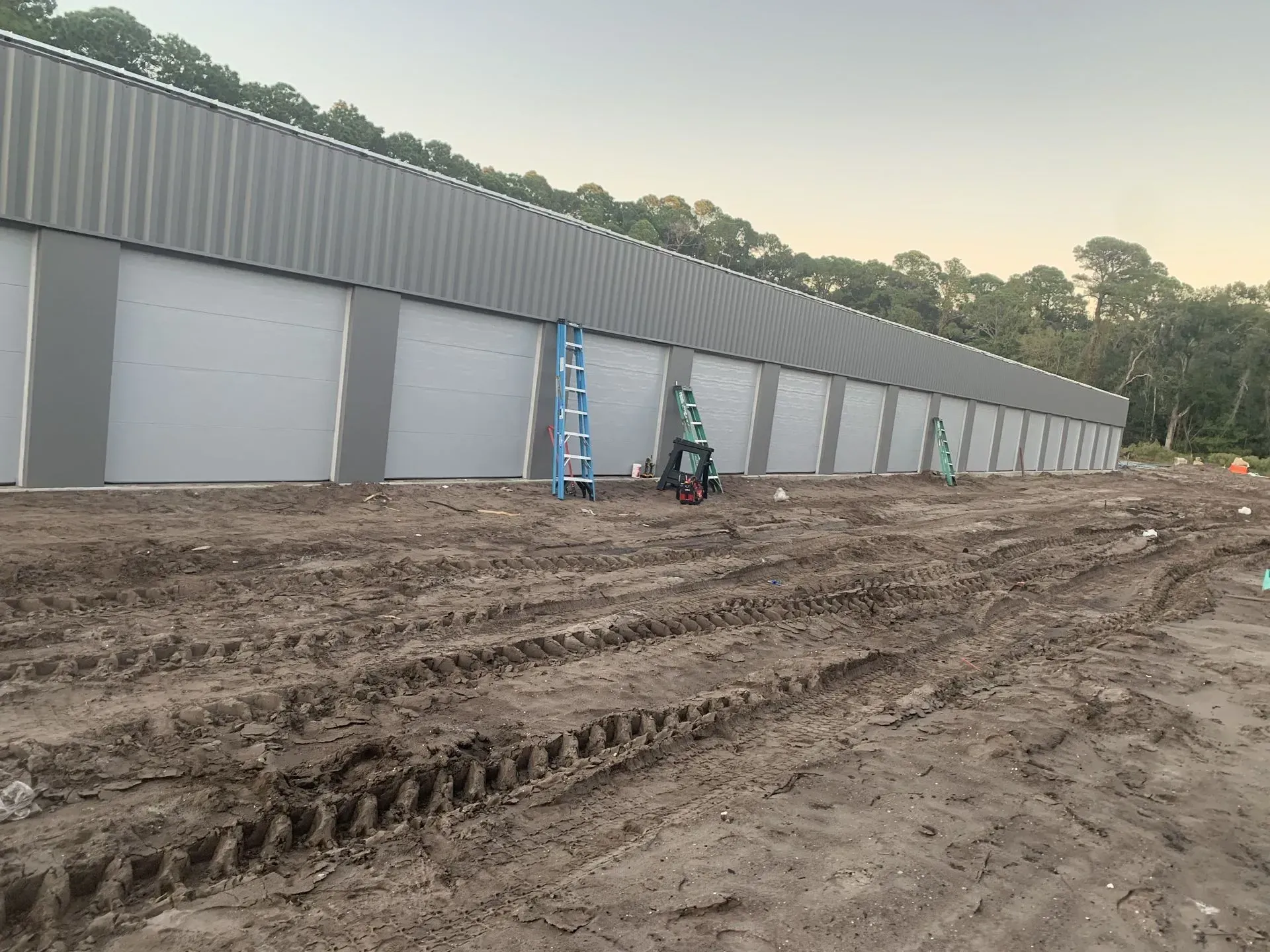 Storage units under construction, with gray doors, dirt, and ladder.