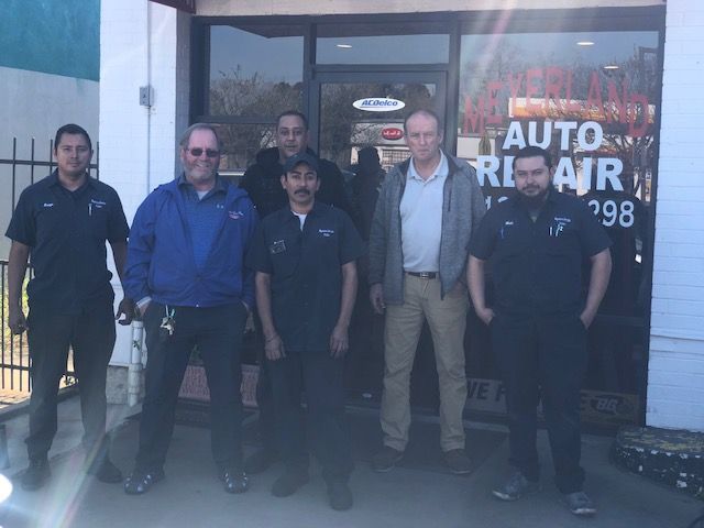 Six people standing in front of an auto repair shop. The sign says 