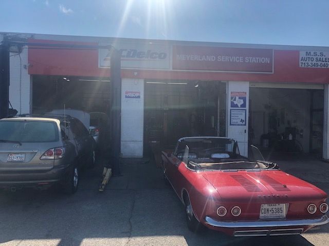 A red convertible parked in front of an auto service station, with a silver SUV to the left. | Meyerland Service Station
