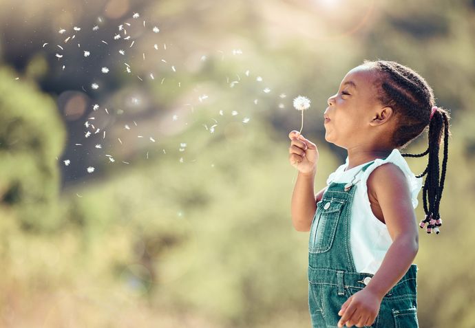 Child in denim overalls blowing bubbles outdoors in soft sunlight