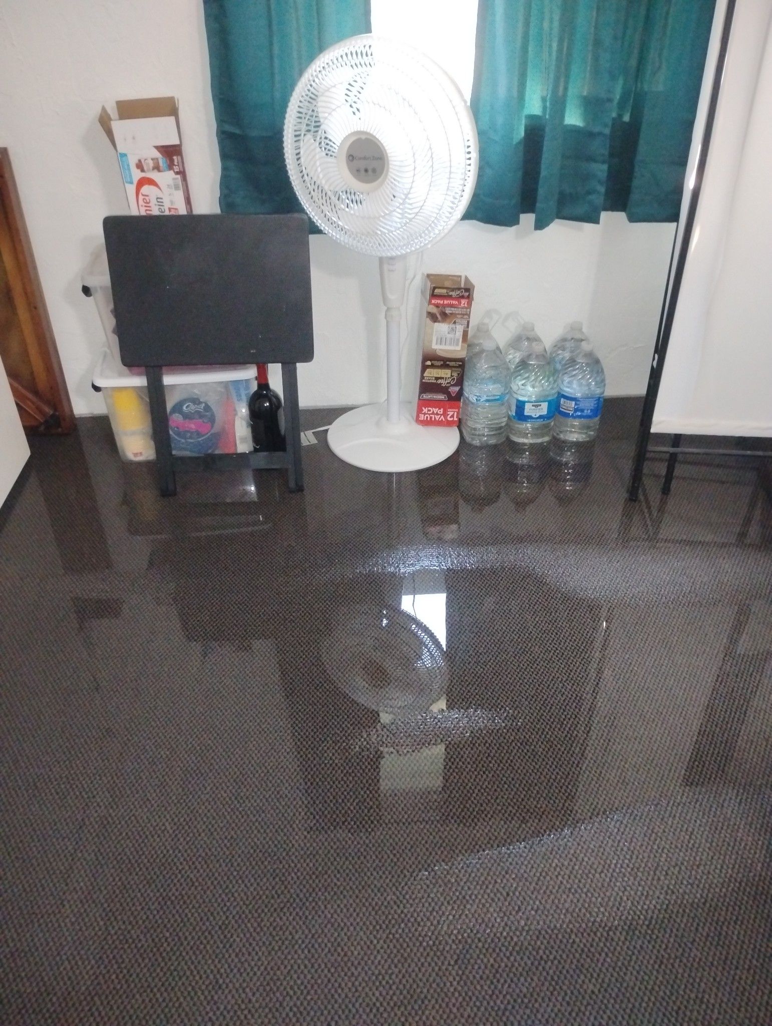 A room with a fan and water bottles on the floor.