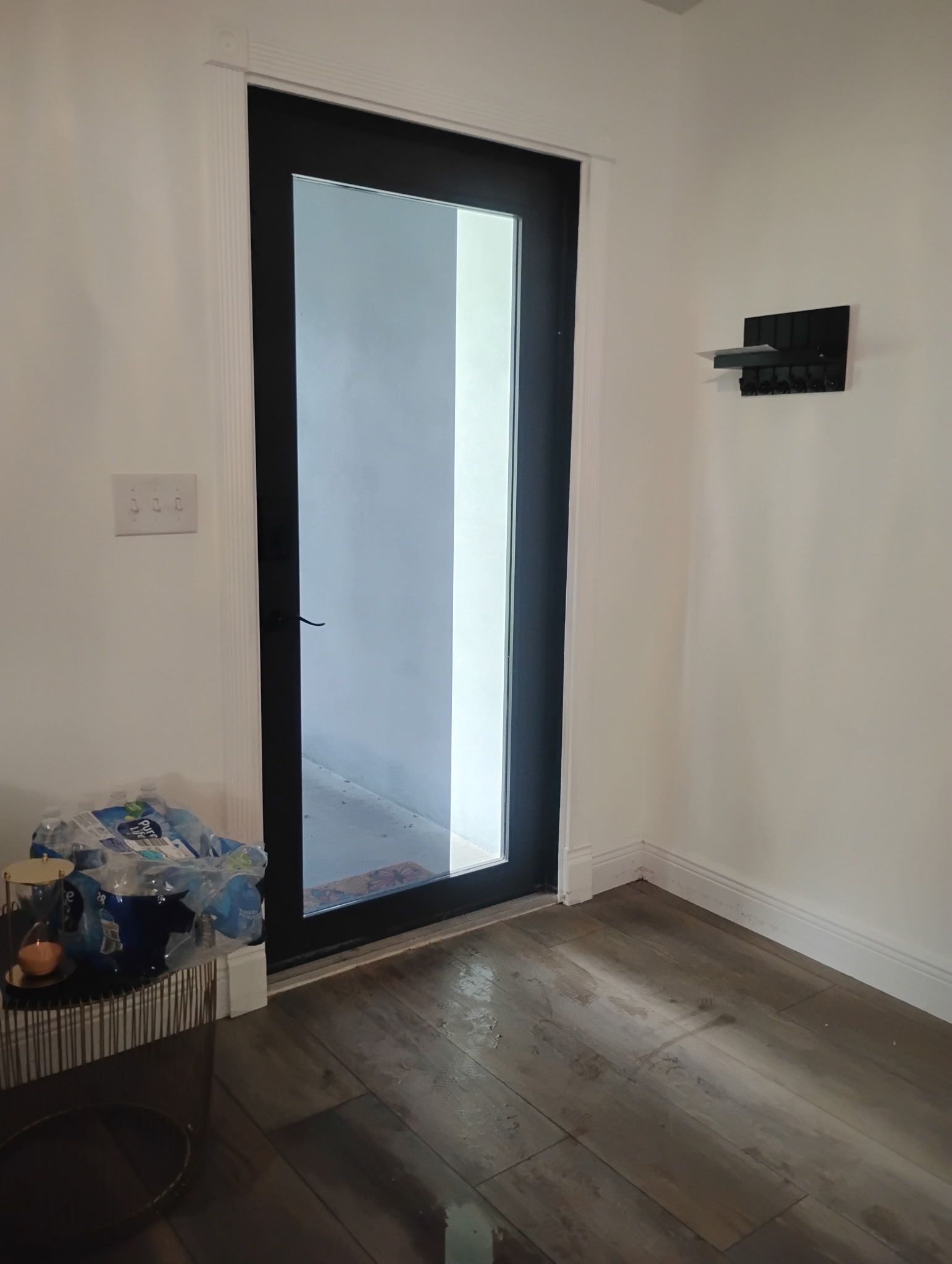 Black door and sconce on white walls. Dark wood floor.