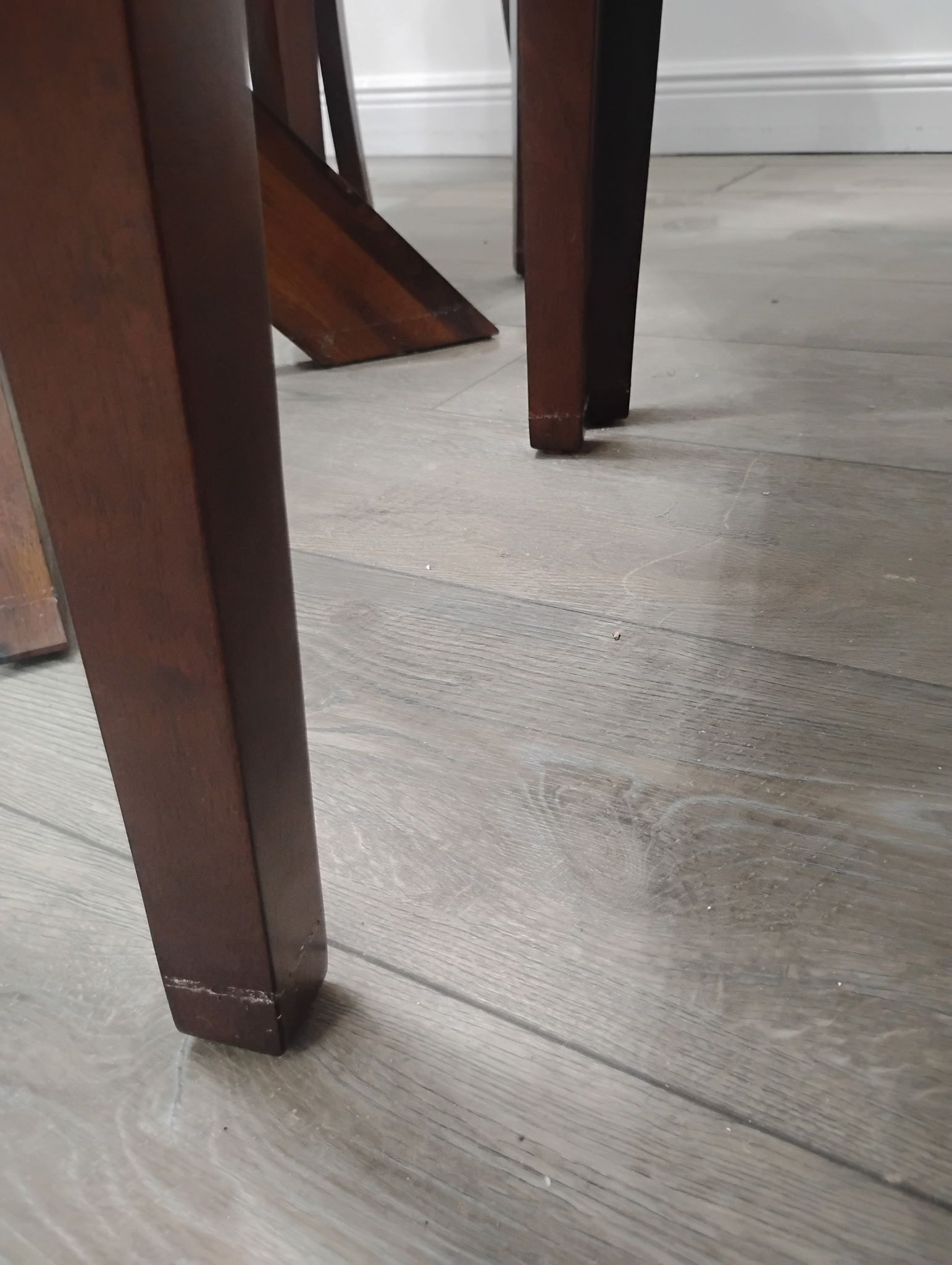 Wooden table legs on a wood-look floor, with a white wall in the background.