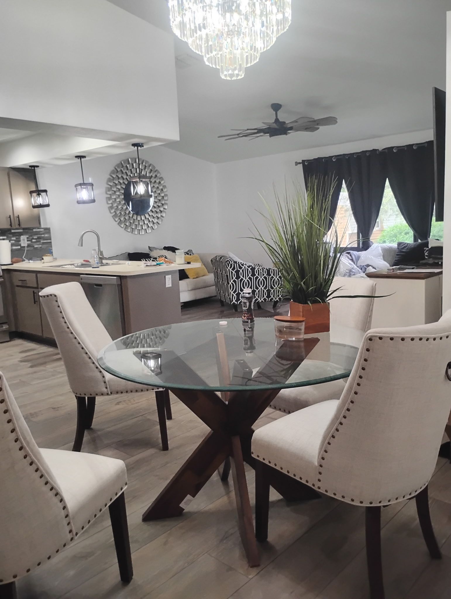 Dining room with a glass-topped table and four beige upholstered chairs. A chandelier hangs above the table.