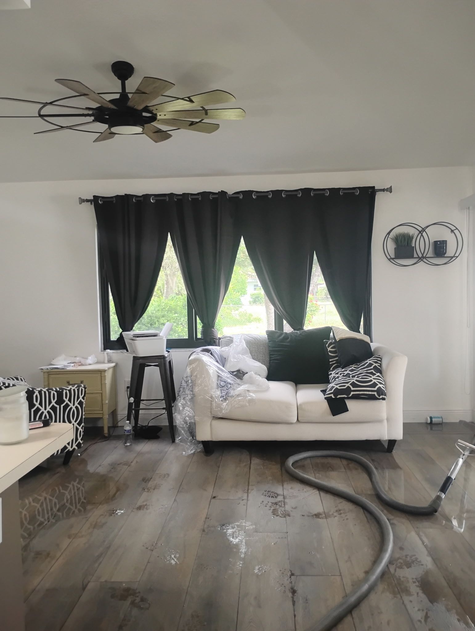 Living room with black curtains, white sofa, and hardwood floor with a vacuum hose.