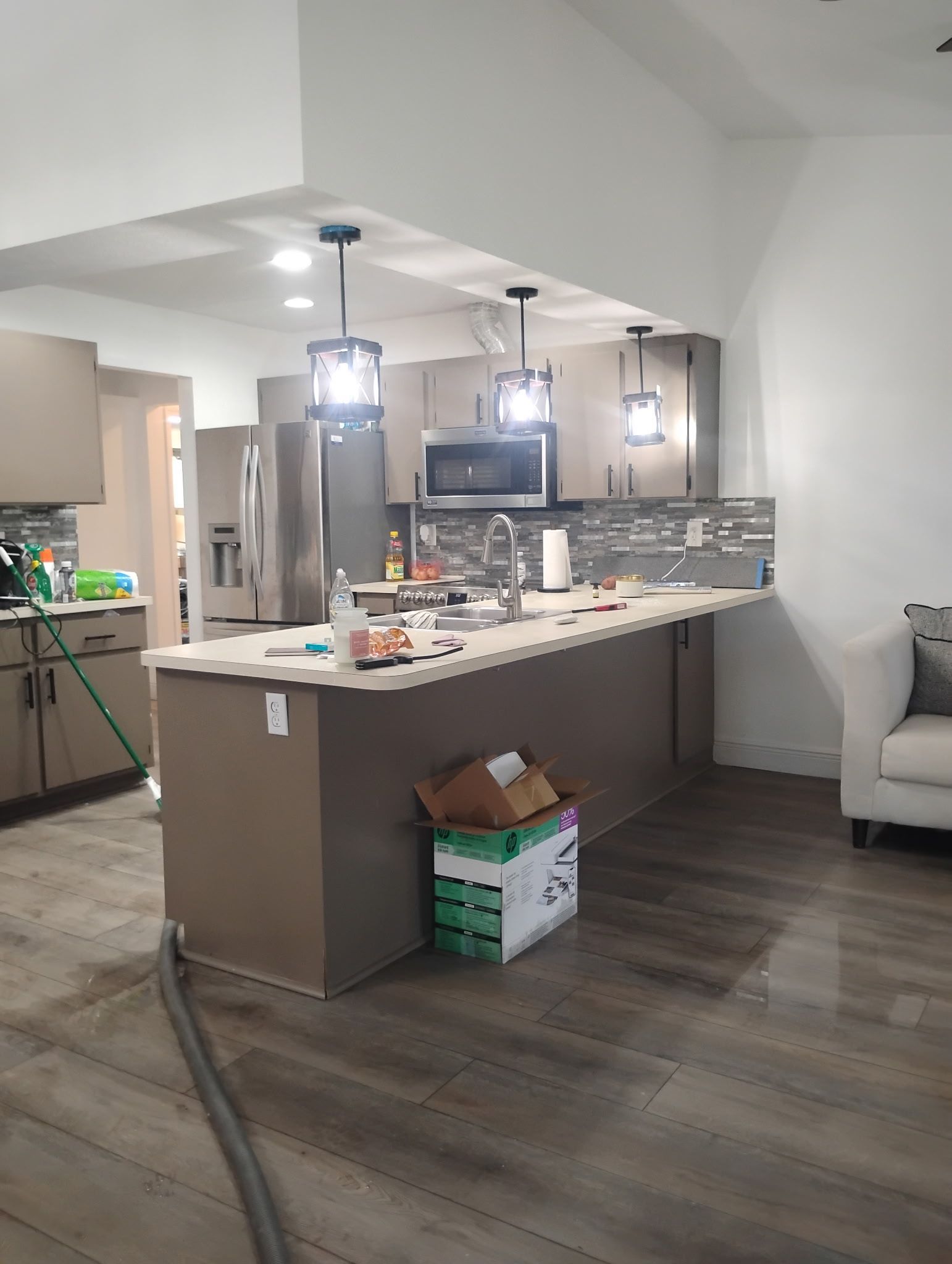 Modern kitchen with island, cabinets, stainless steel appliances, and wood-look flooring.