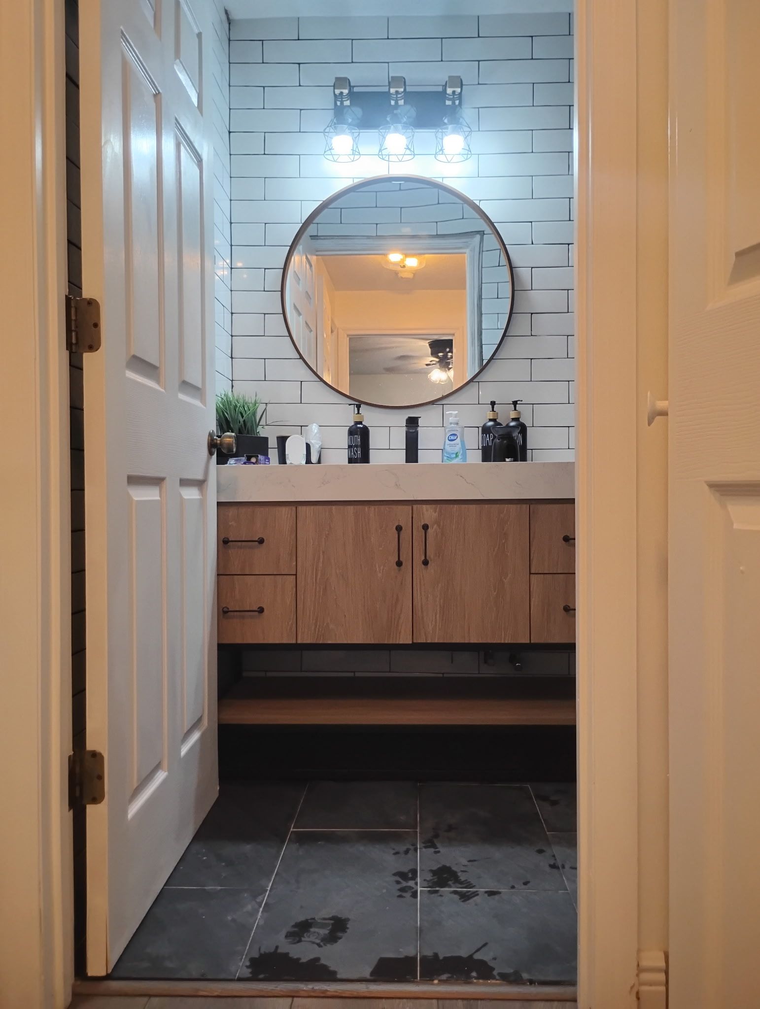 Bathroom interior with wooden vanity, oval mirror, and patterned wall behind the sink.