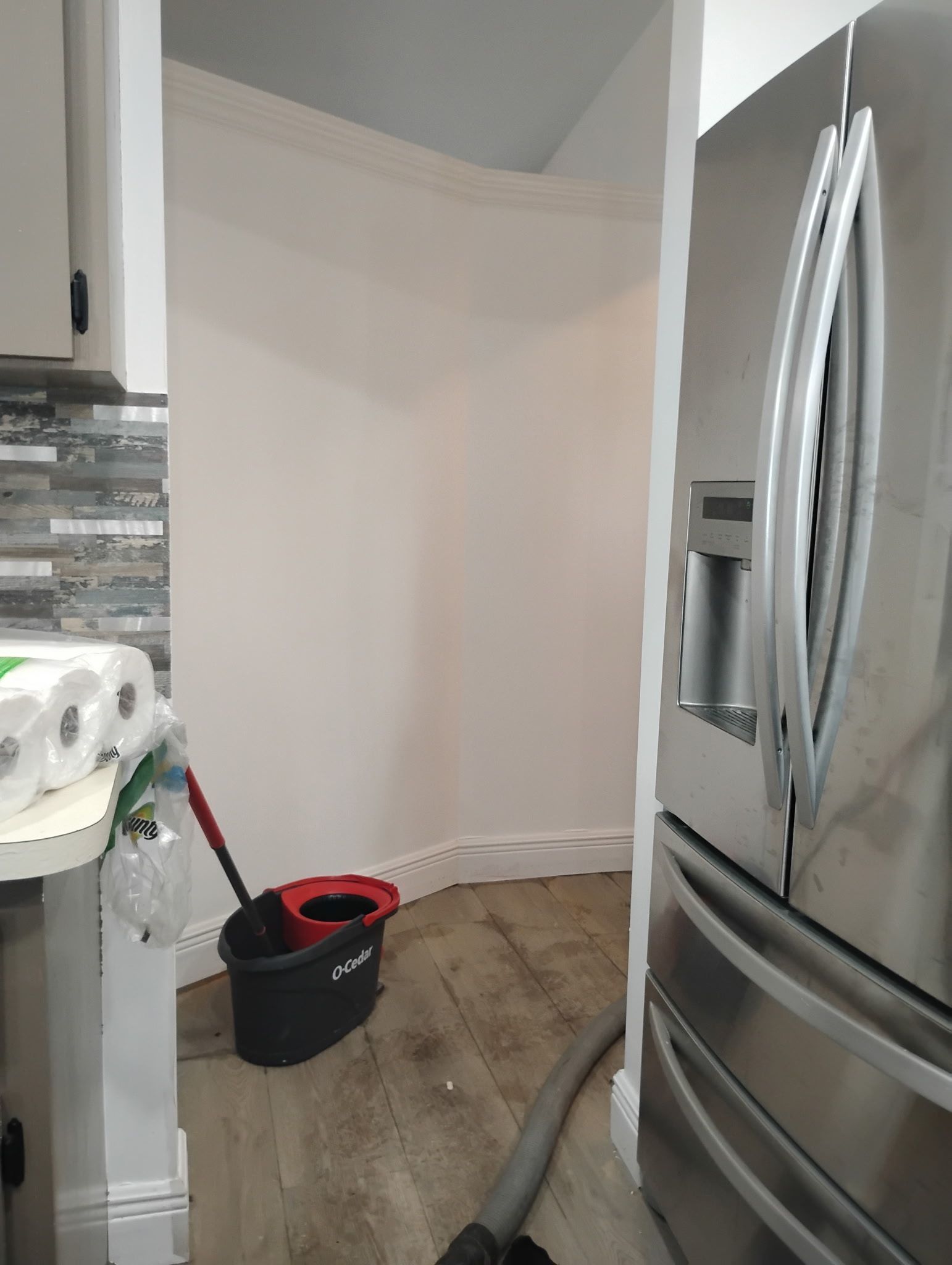 A small alcove with a mop bucket, next to a refrigerator, and a roll of paper towels on a counter.
