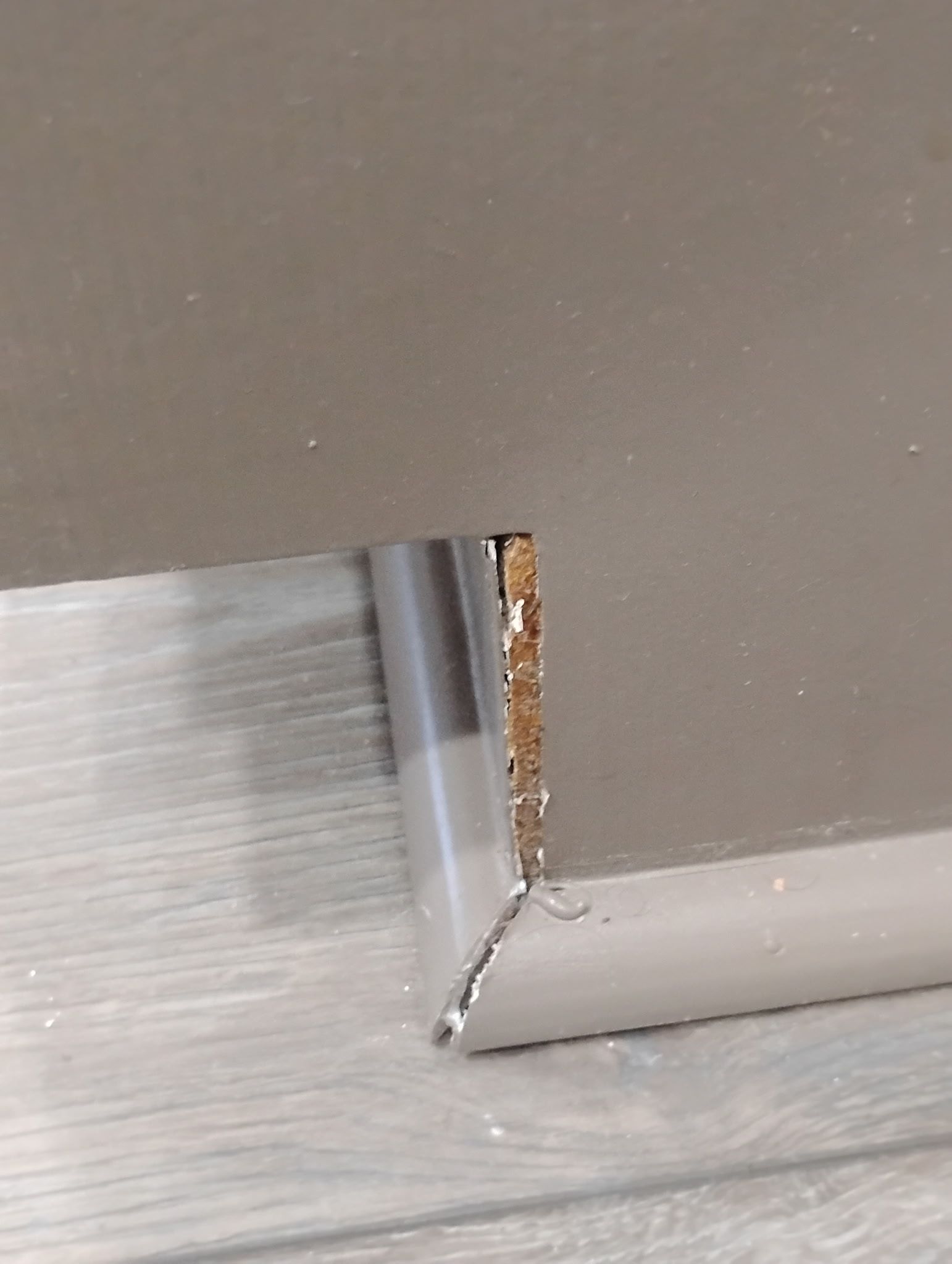 Gray baseboard corner with a gap, installed on gray wall over light wood-look flooring.