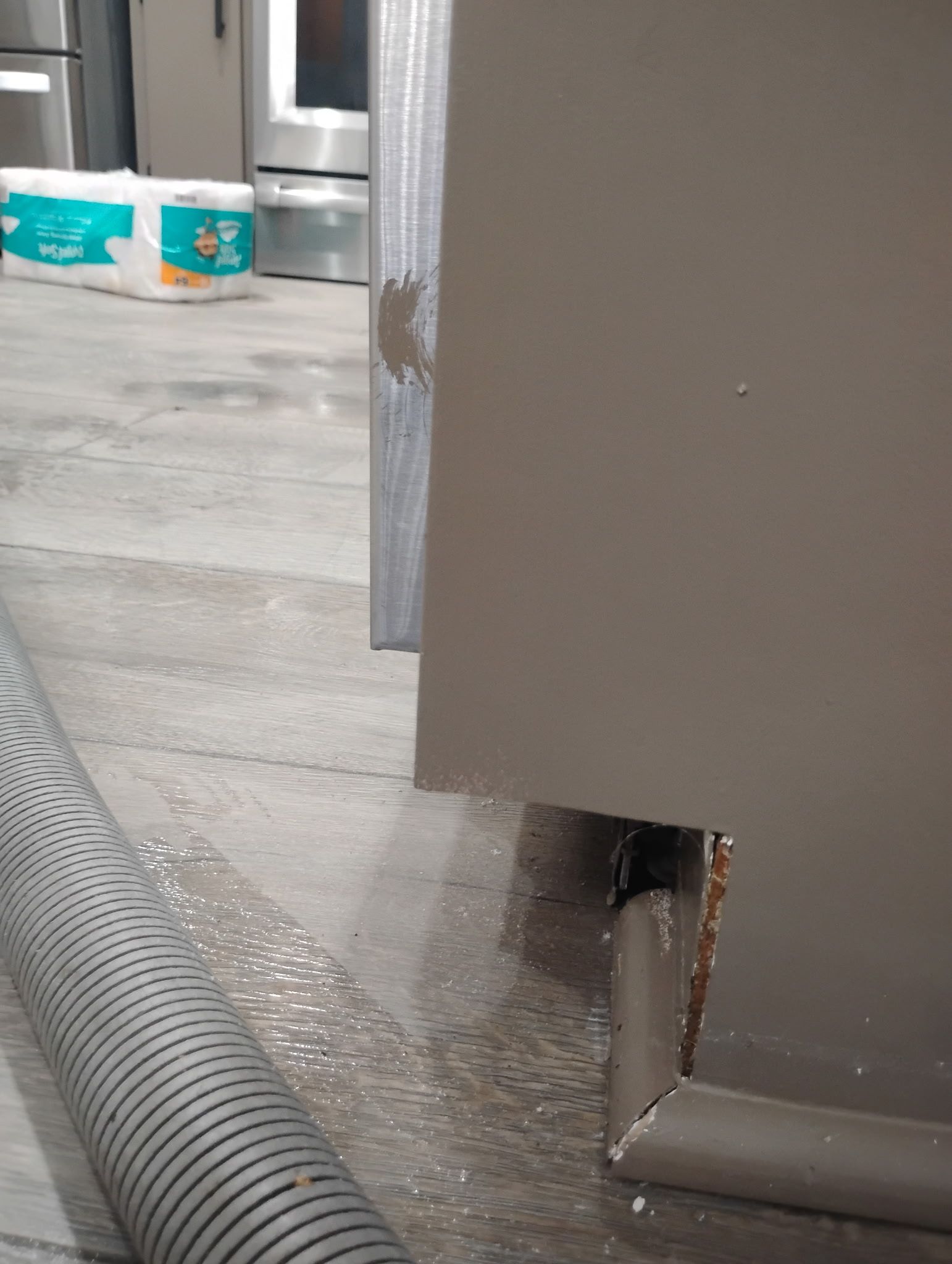 A flooded floor with a hole in a brown cabinet. A vacuum hose and paper towels are in the background.