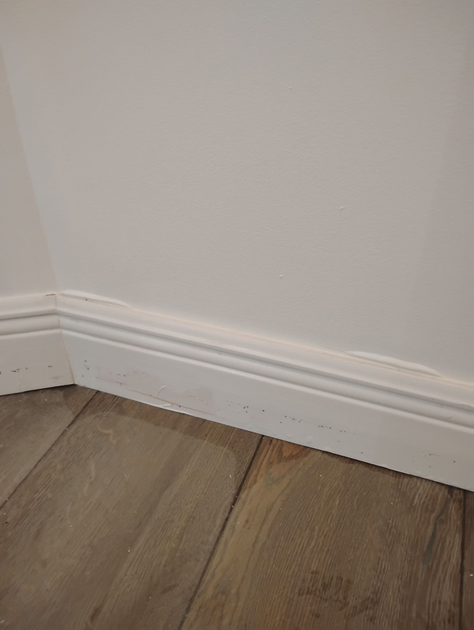 White baseboard trim on a white wall, corner with wooden floor.
