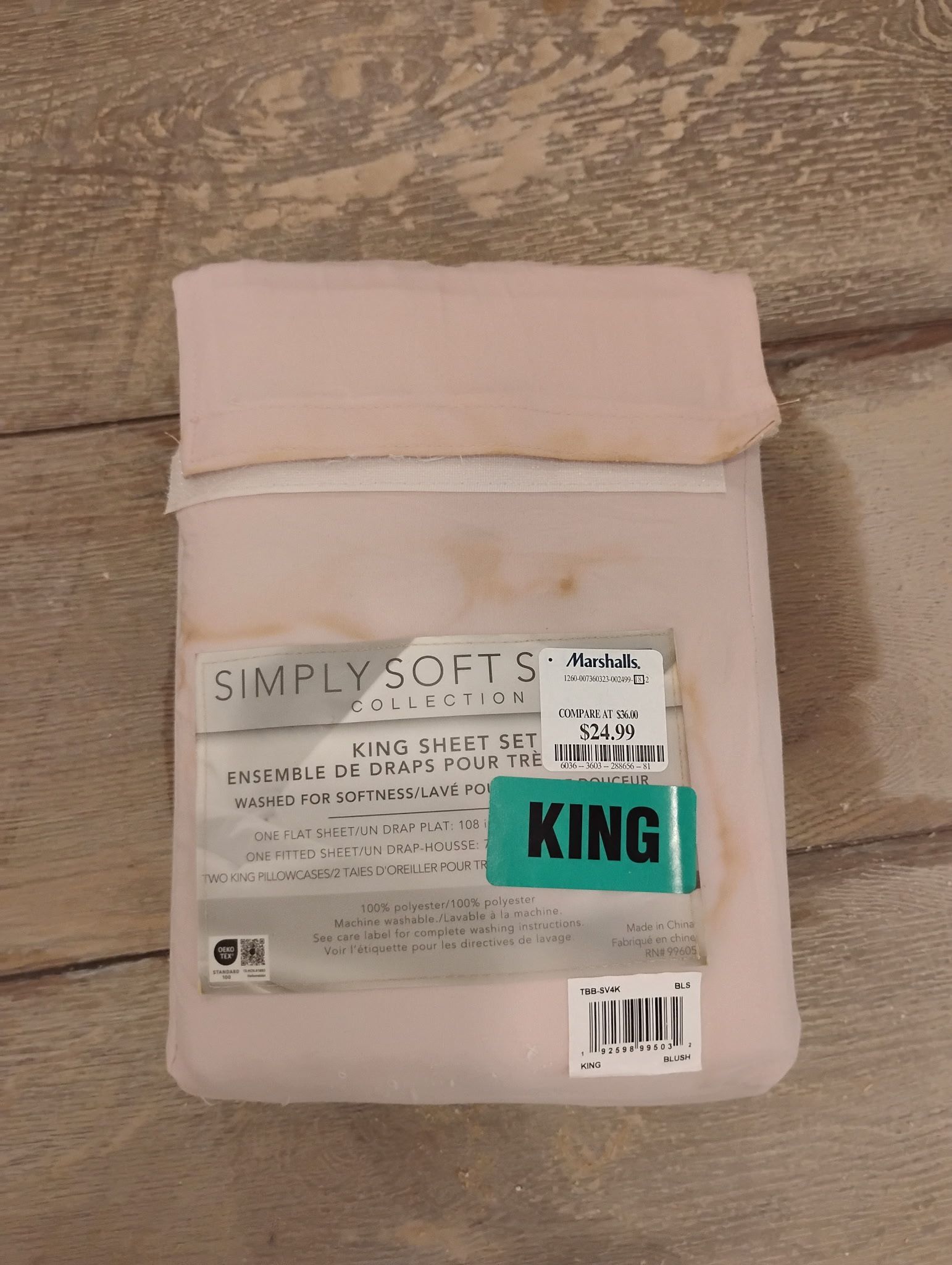 Pink king-sized Simply Soft sheet set packaging on a wood floor.