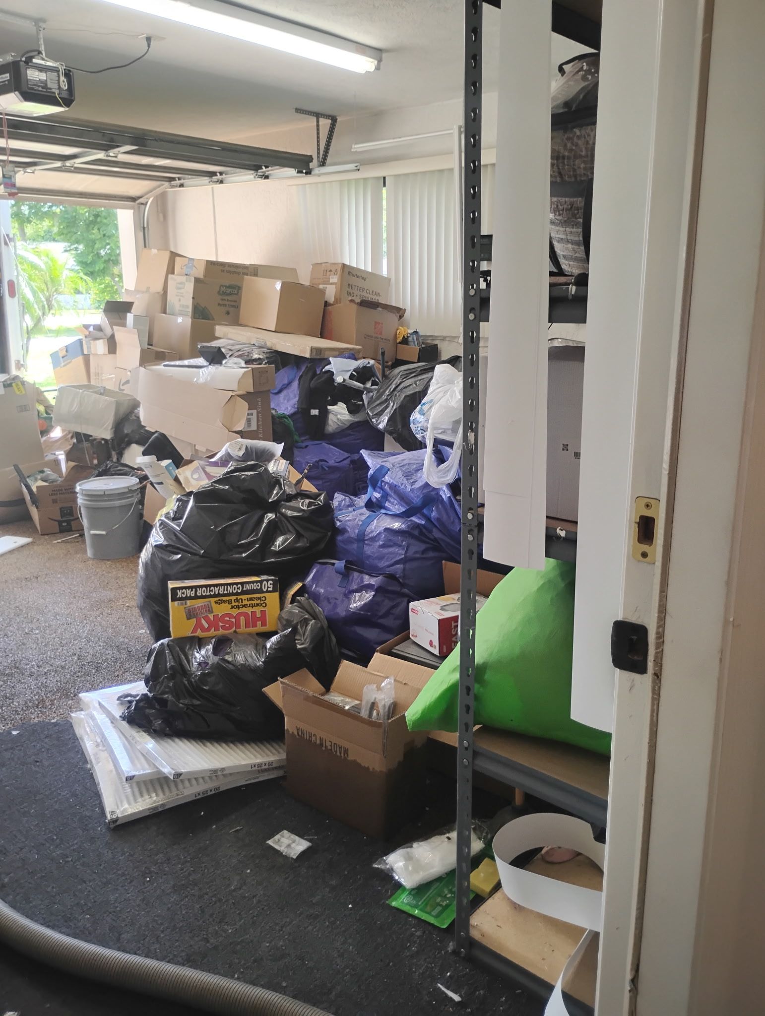 Garage filled with boxes, trash bags, and clutter; door partially visible.
