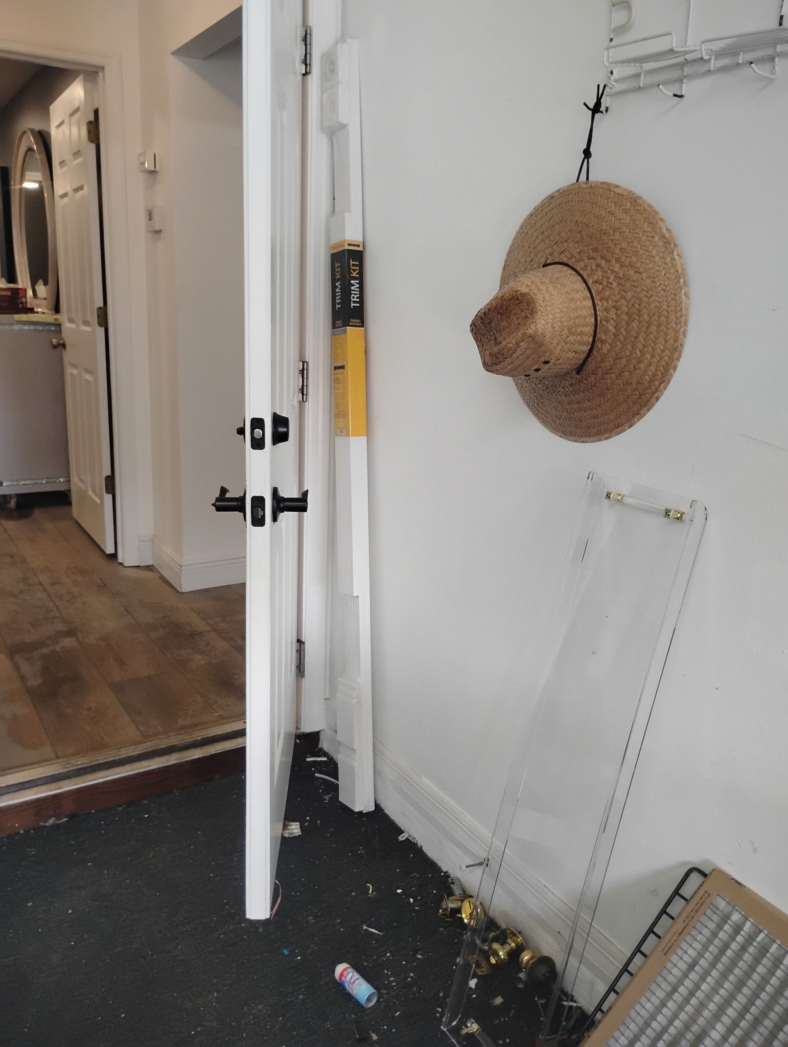 White door propped open in a doorway, next to a wall with a hat hanging on it and debris on the floor.