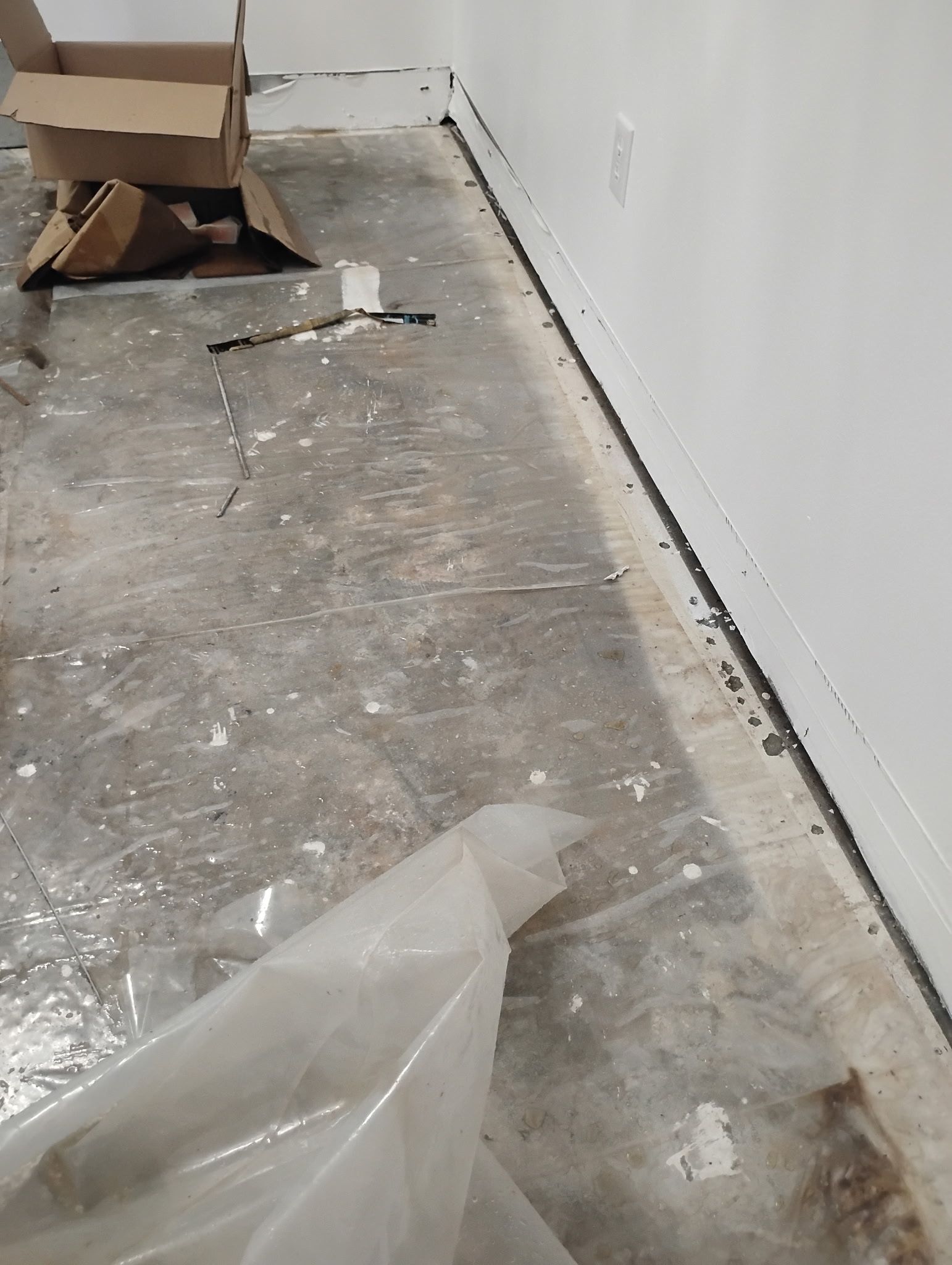 Gray concrete floor with debris, white walls, and a plastic sheet.