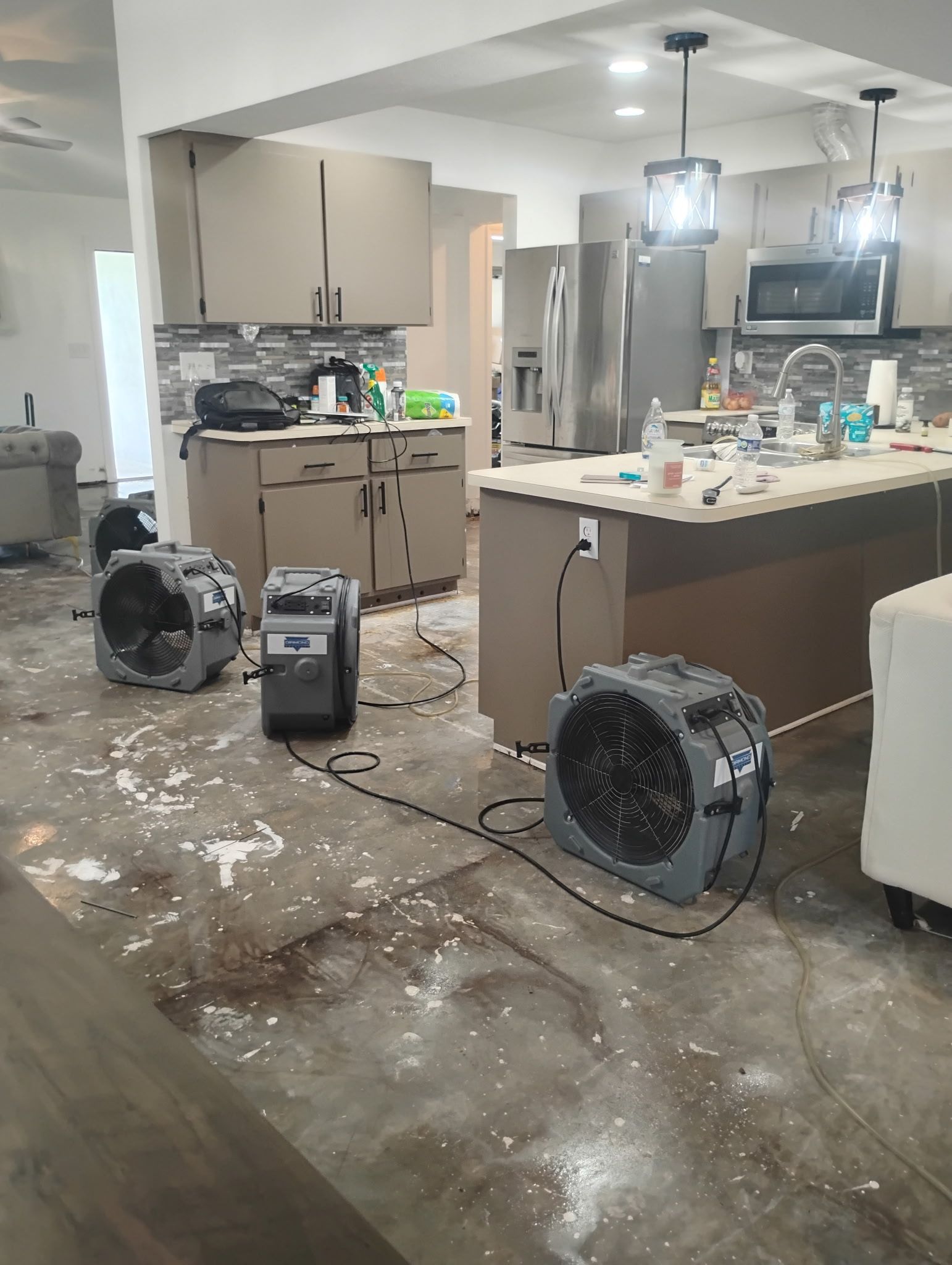 Three air movers drying a flooded kitchen with damaged flooring and cabinets.
