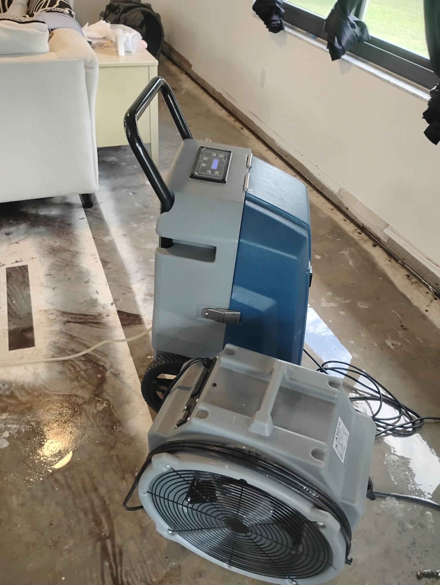 Dehumidifier and fan on a wet floor, likely after water damage.