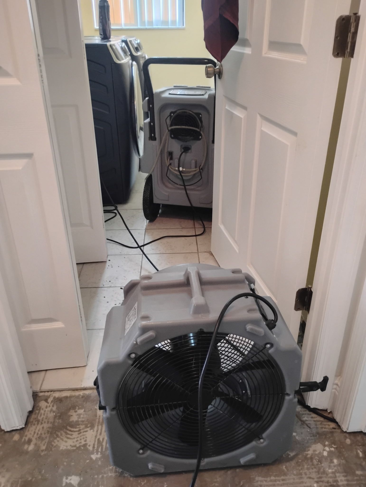 Two gray air movers in a hallway, drying out the floor. White doors flank the hallway. A washer is visible.