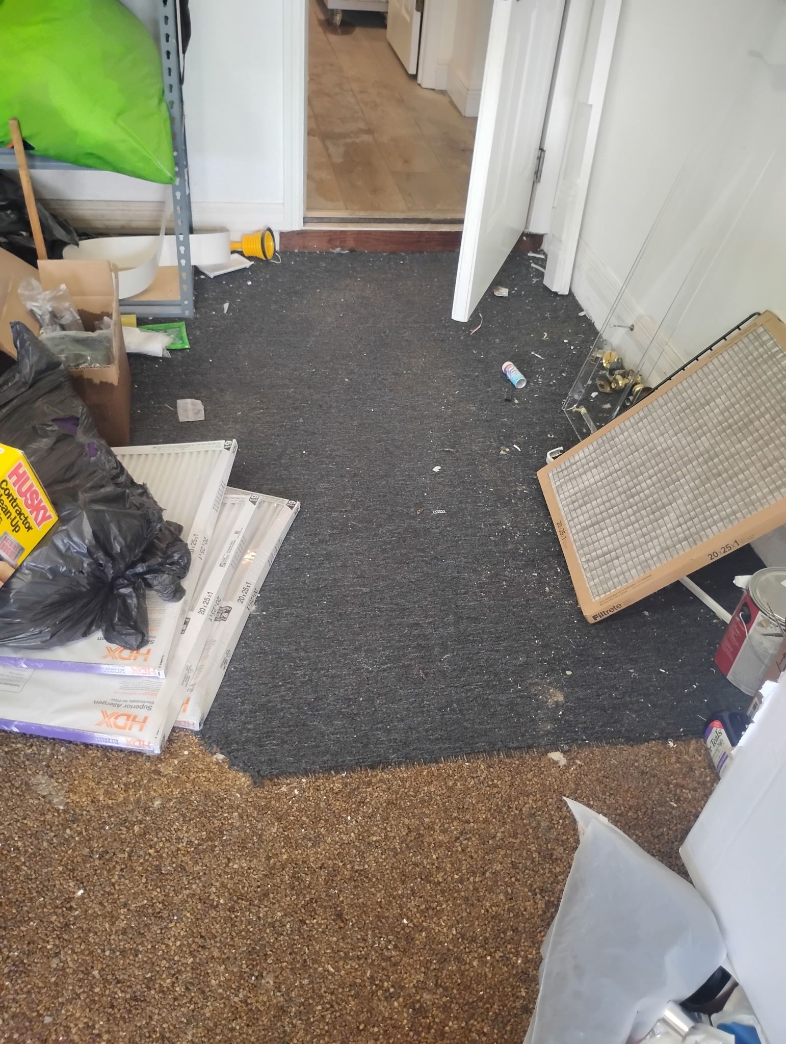 Cluttered room with debris, dark mat, and doorway. Materials, trash, and an air filter are visible.