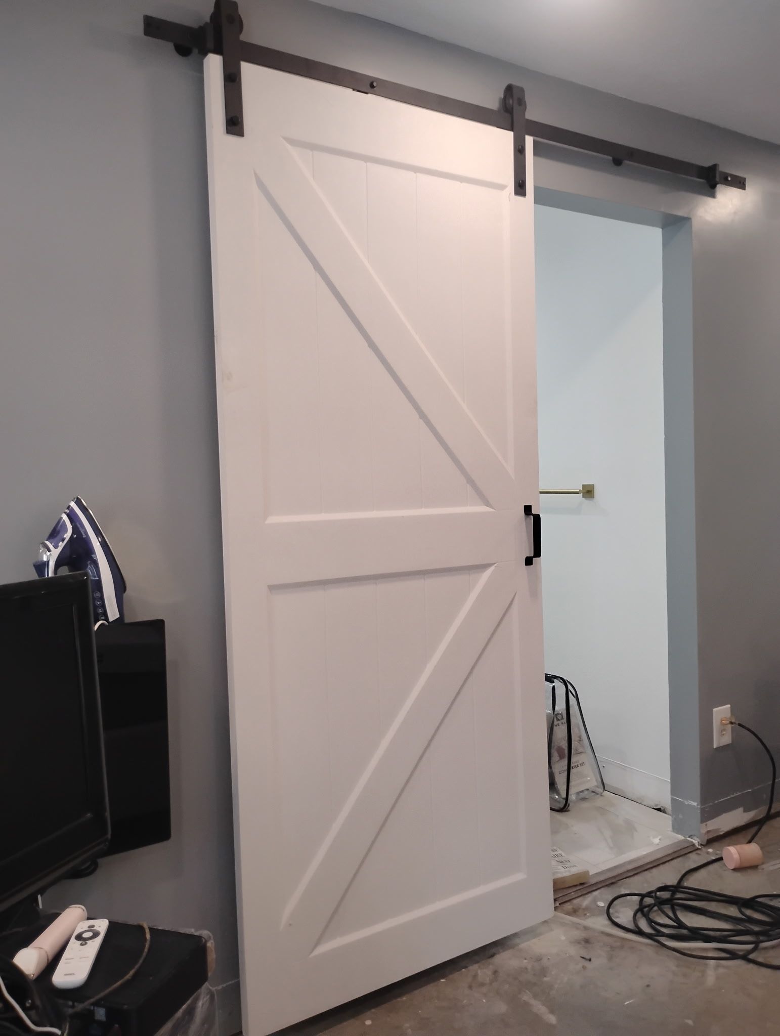 White barn door on a sliding track, open to a room with gray walls.